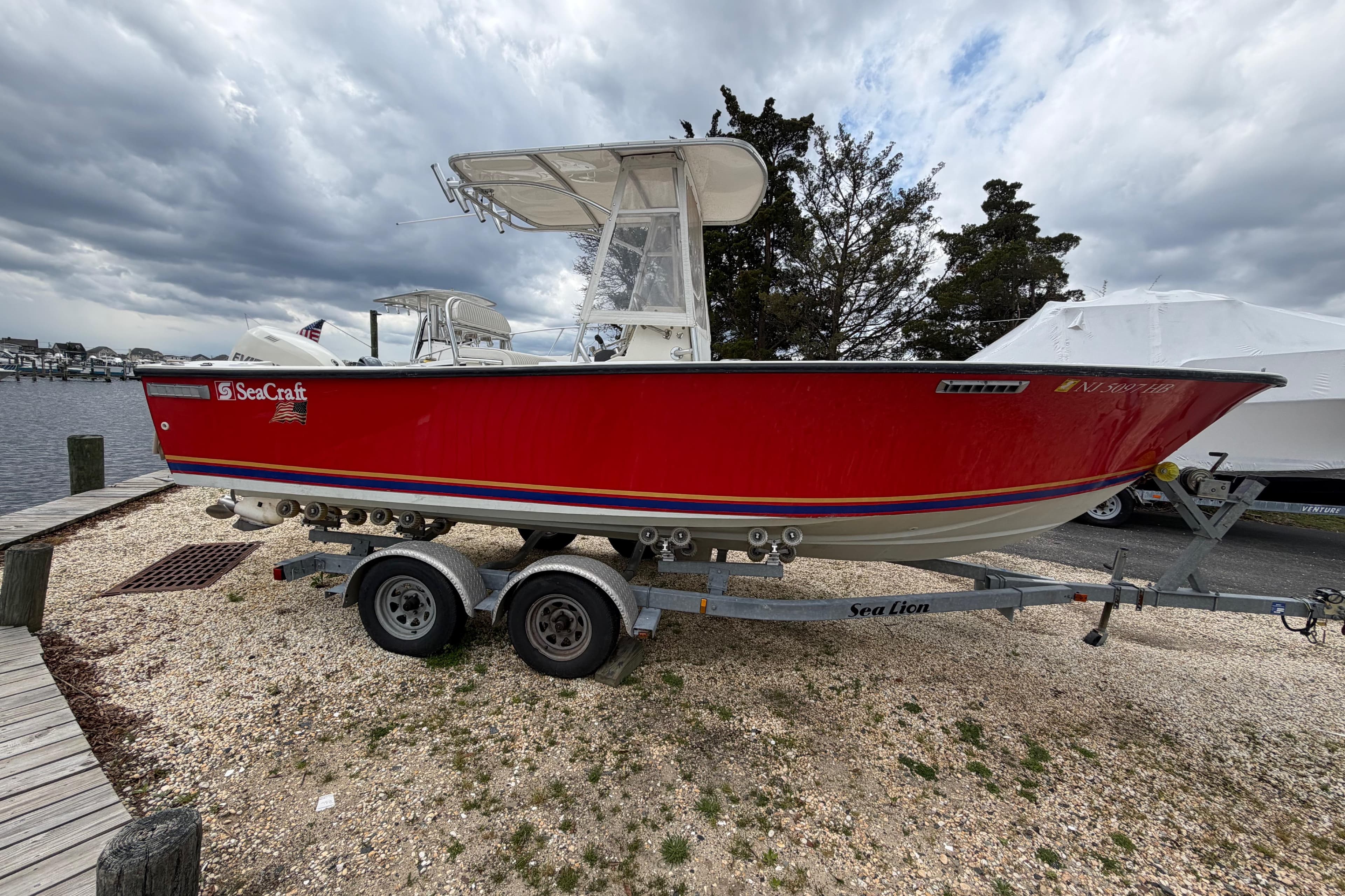 1985 SeaCraft SC 23 Classic boat on trailer, red hull, dockside setting.