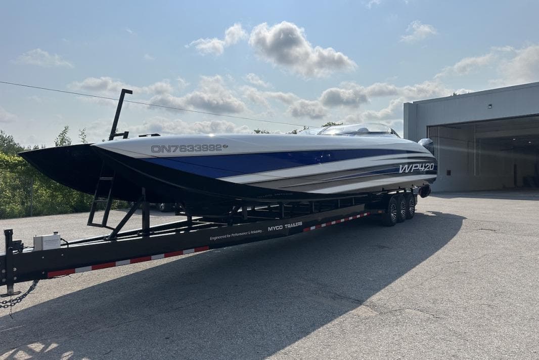 2018 Wright Performance 420 boat on trailer, parked outside a garage under a cloudy sky.