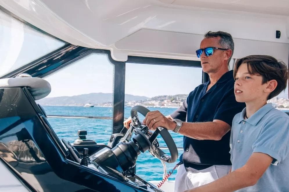 Man and boy steering Beneteau Antares 12 Coupe 2026 on the sea.