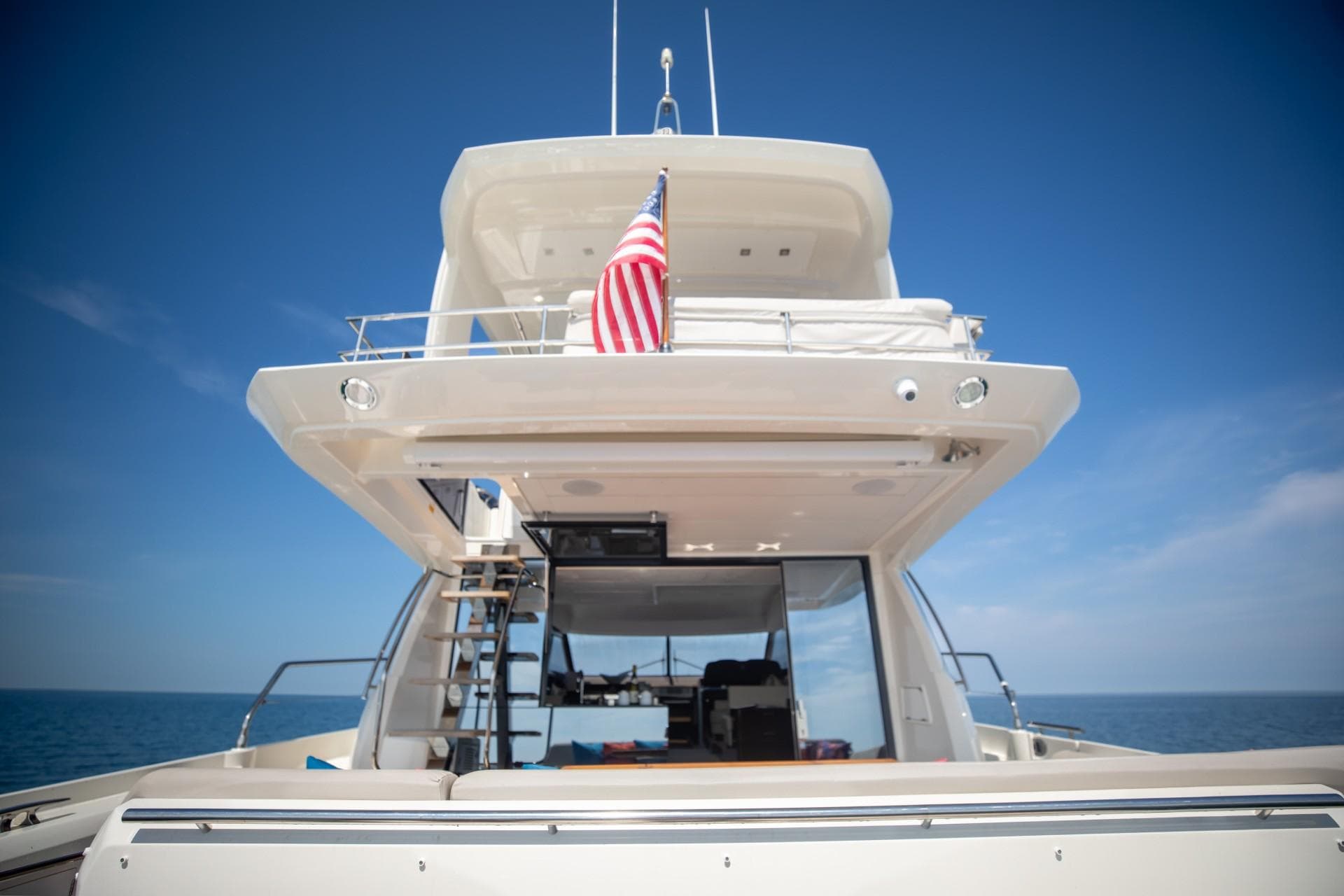 2020 Prestige 590 Flybridge Cruiser on open sea, rear view with American flag.