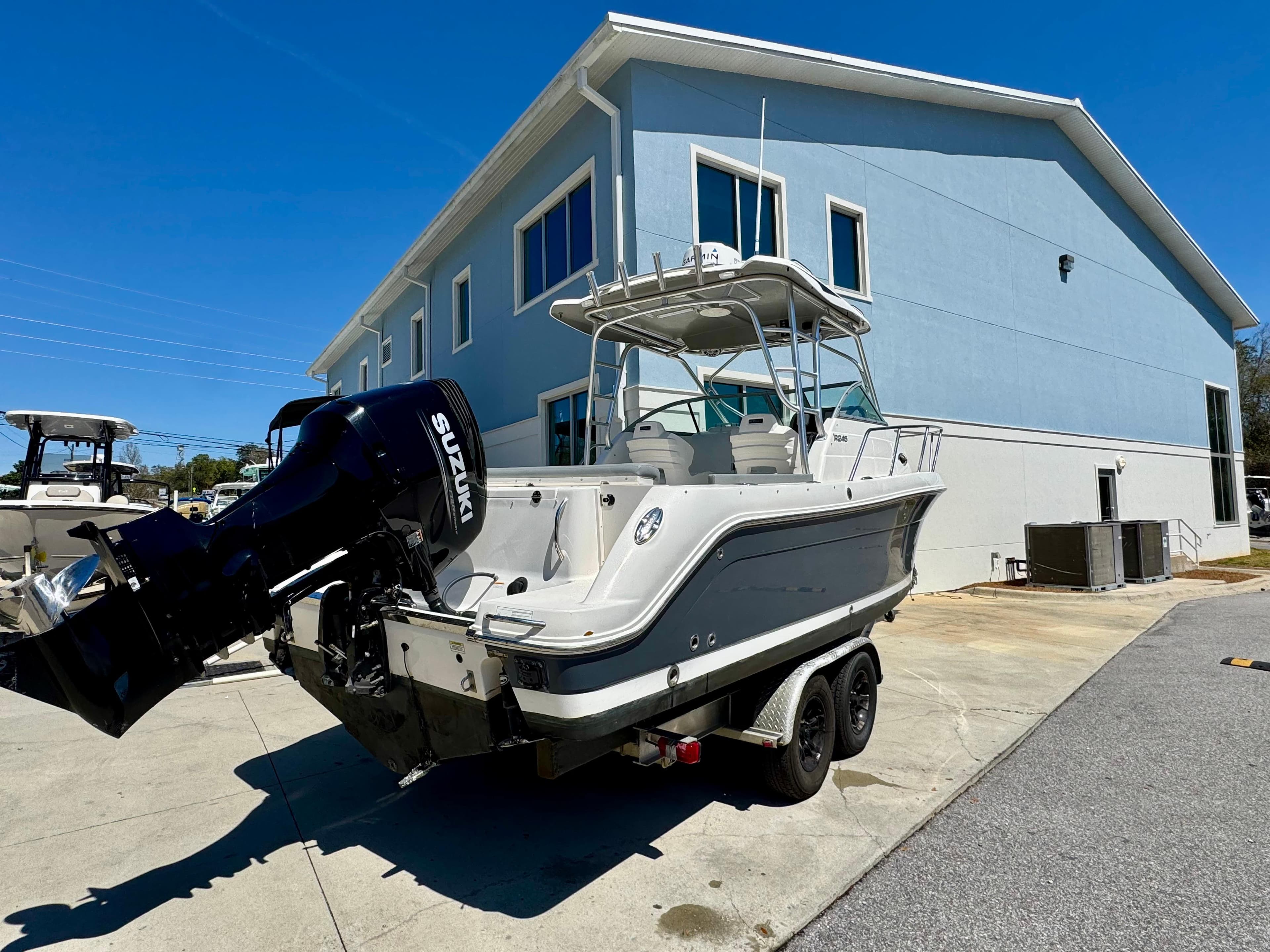 2015 Robalo R245 Walkaround boat with Suzuki outboard motor, parked near a blue building.