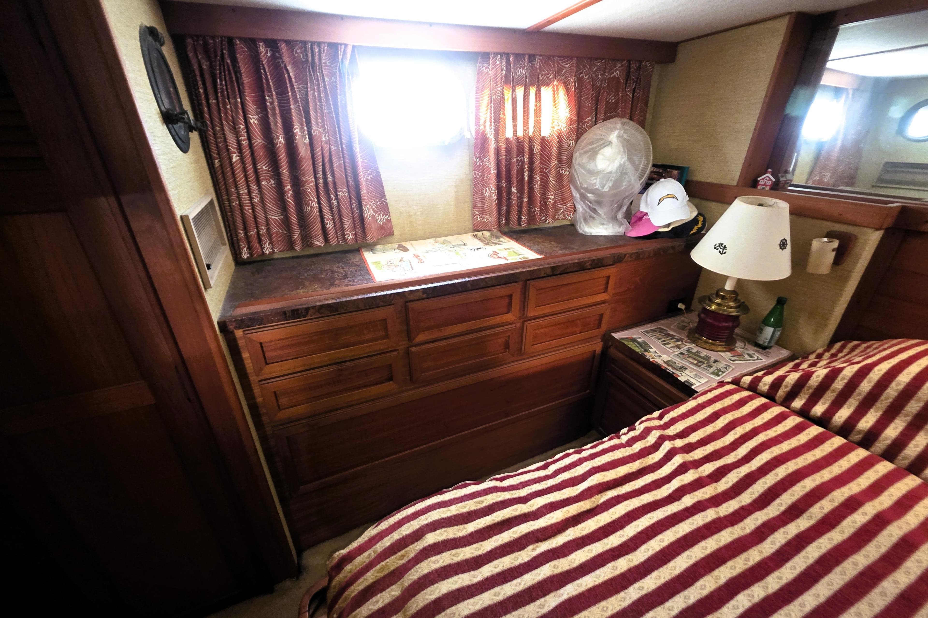 1979 Trojan 44 Motor Yacht interior with striped bedding, wooden cabinetry, and decorative lamp.