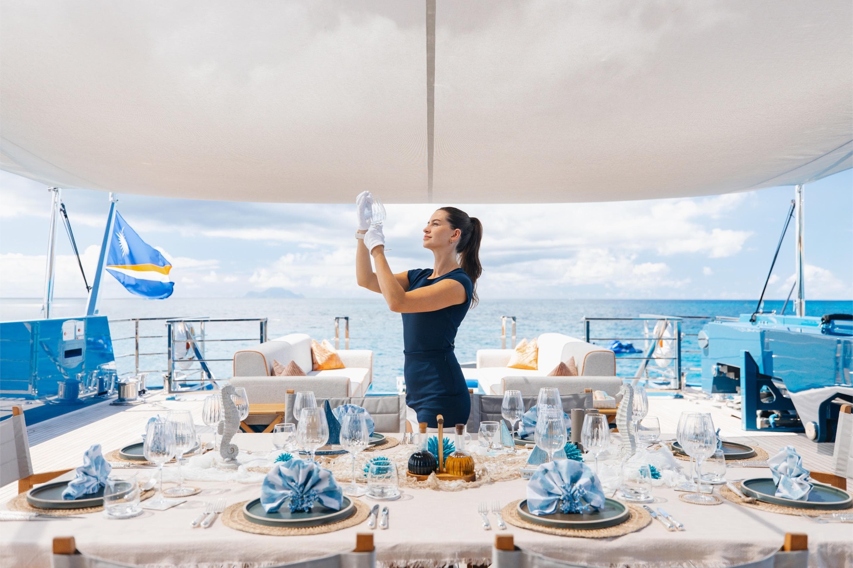 Luxury dining setup on 2024 Dunya Yachts Explorer, with crew member preparing table.