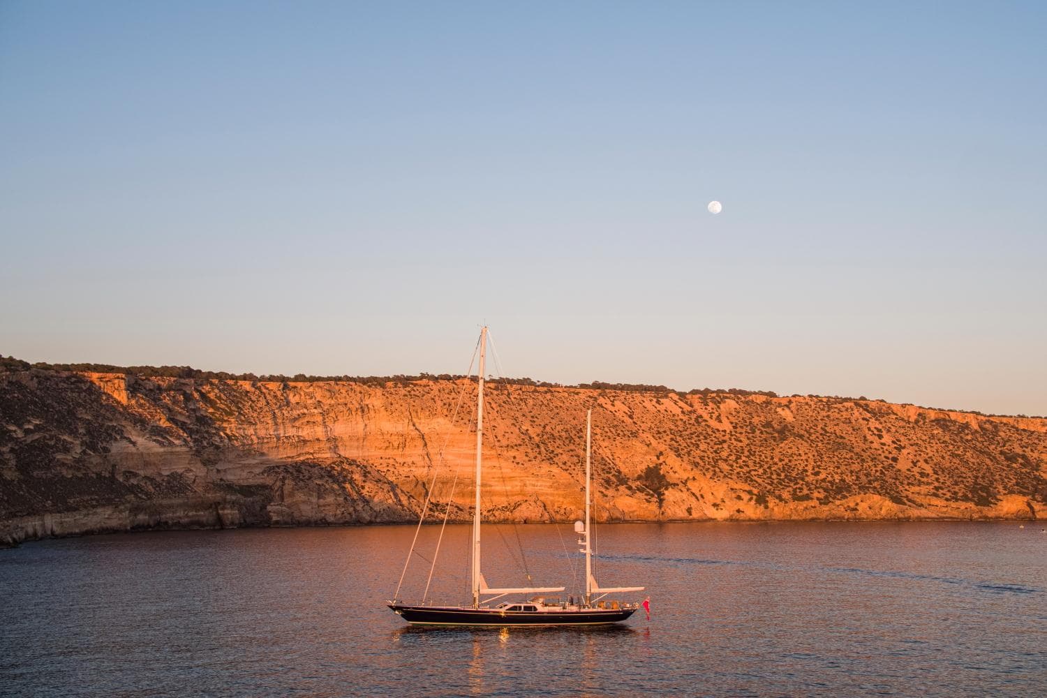 Alloy Yachts Cruising Ketch 1998 near rocky coastline at sunset.