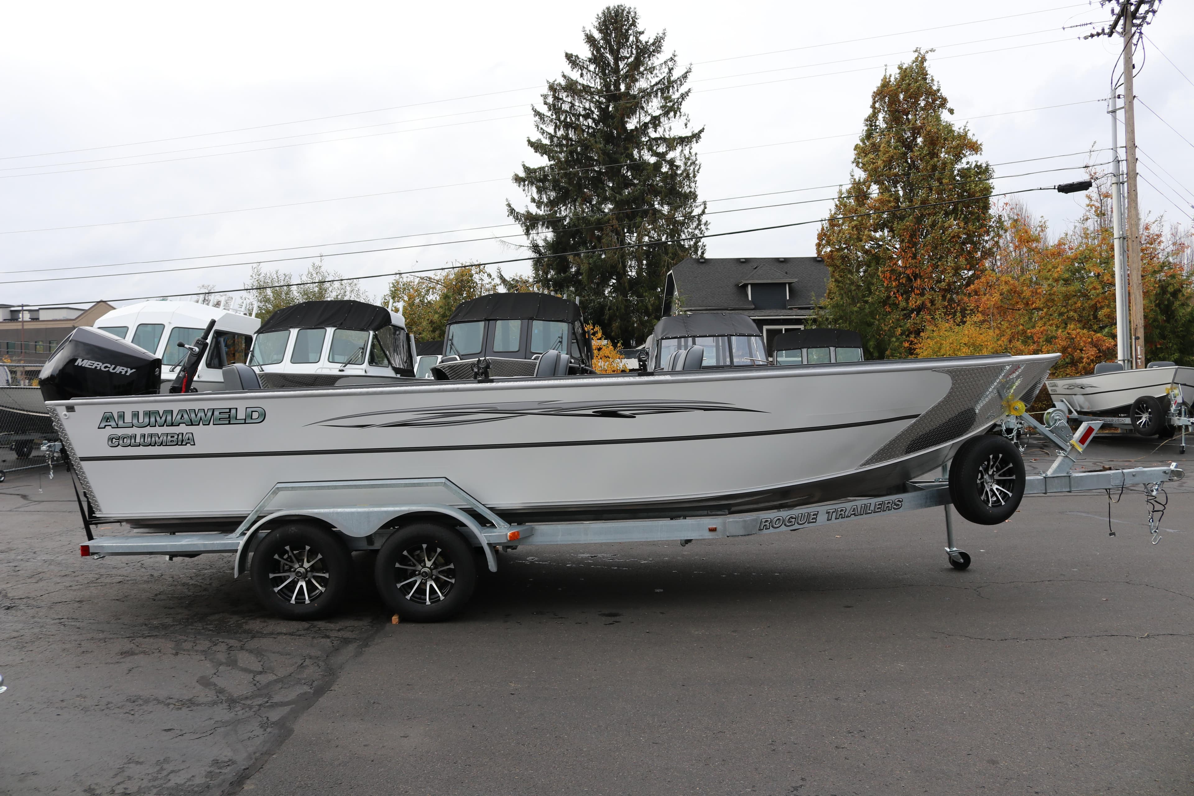 2026 Alumaweld Columbia 23 boat on trailer, parked outdoors with autumn trees.