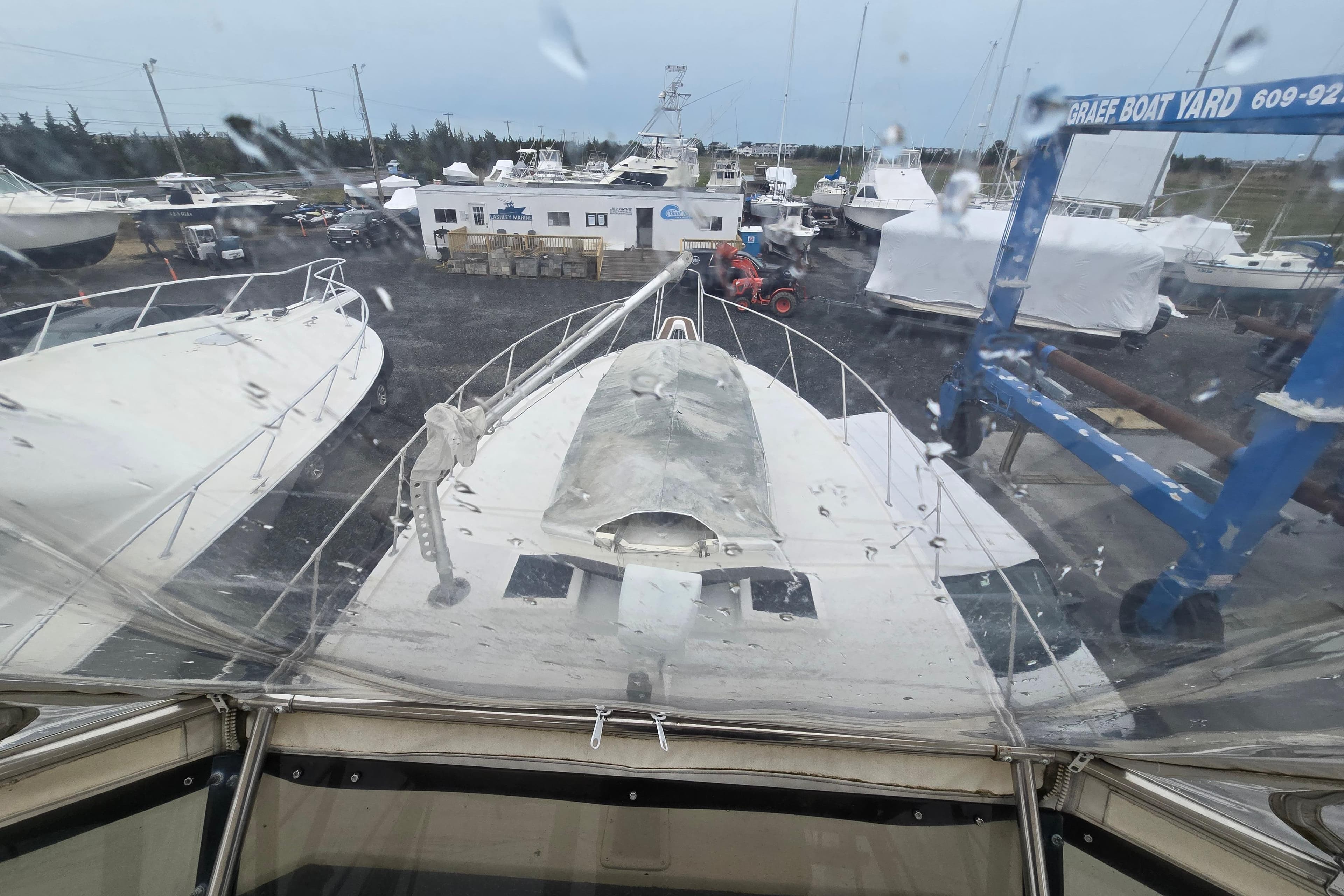1975 Hatteras 46 Convertible yacht in boatyard, rainy day, surrounded by other vessels.