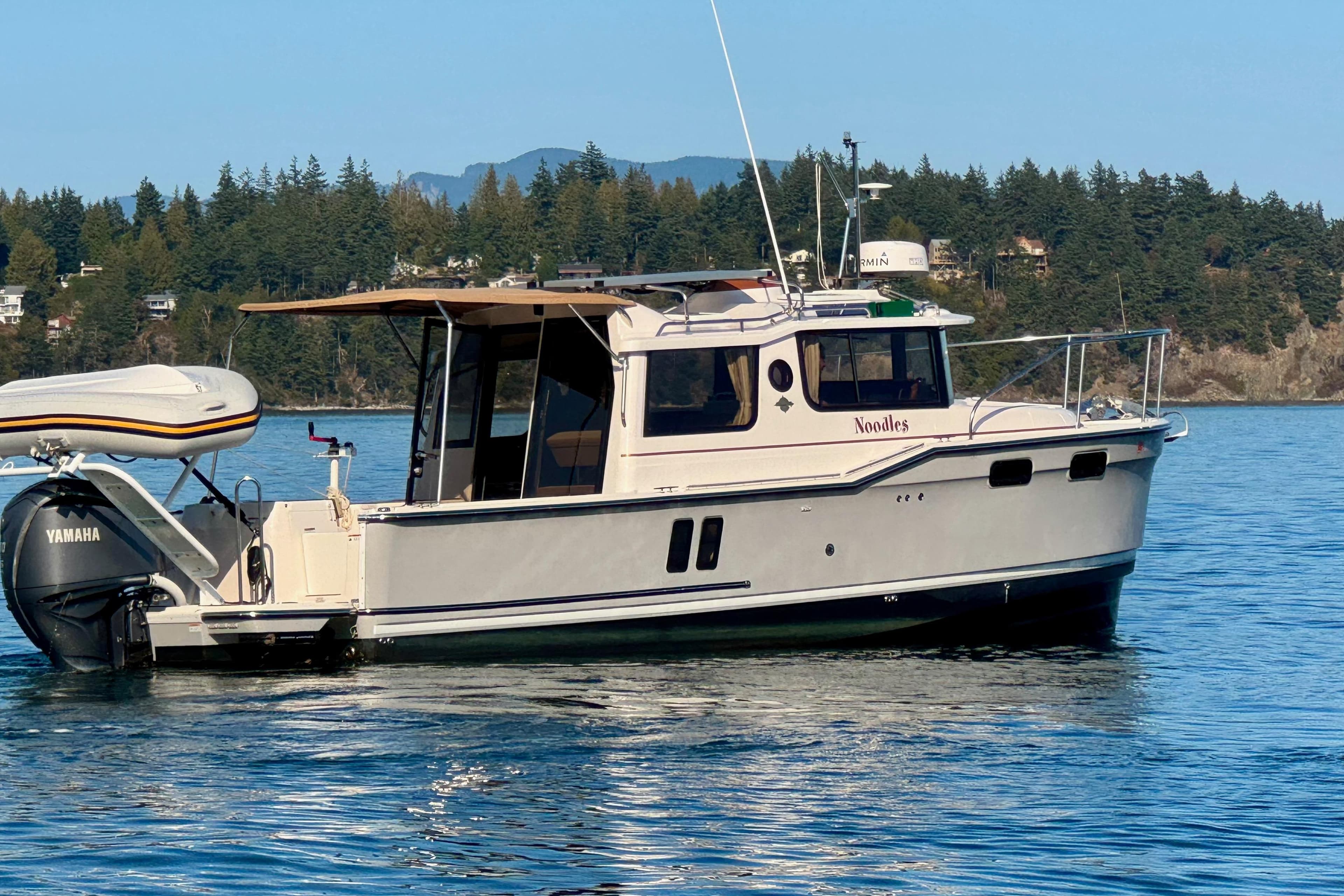 2024 Ranger Tugs R-27 boat on calm water with scenic forested background.