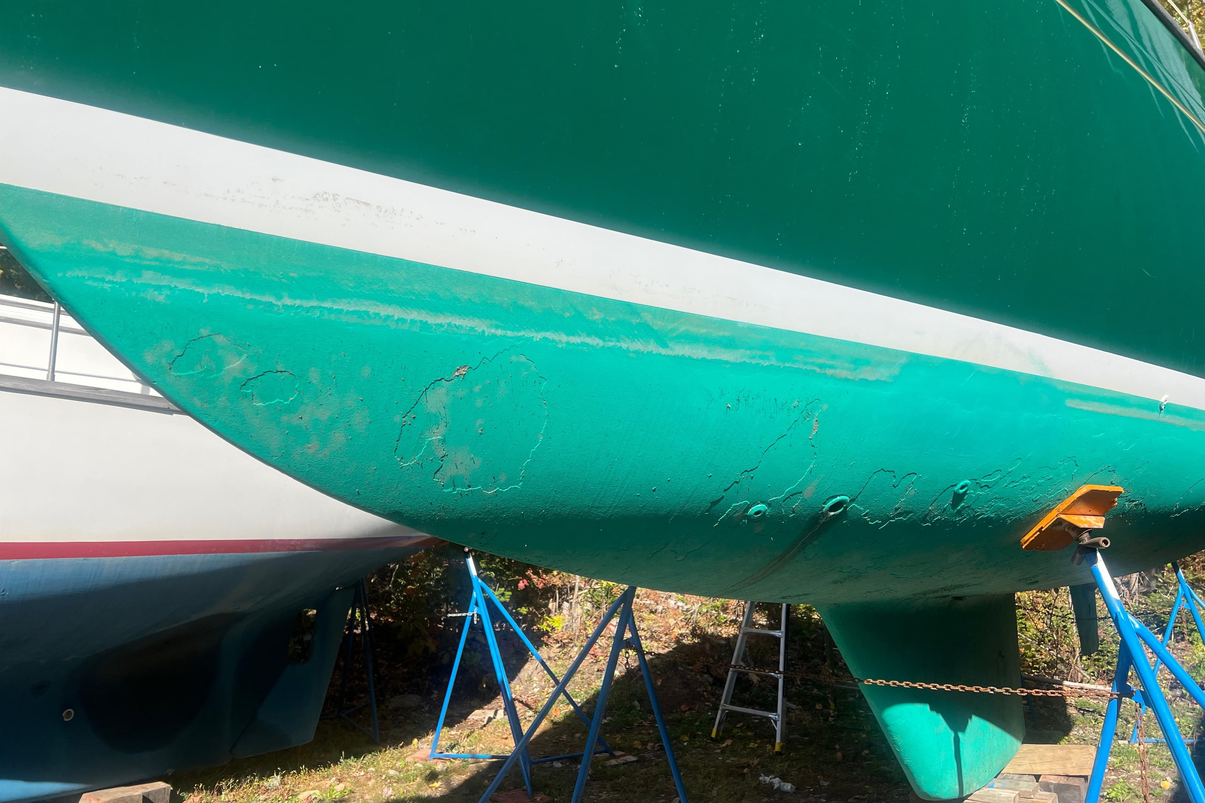 Green hull of 1986 Victoria 34 Sloop sailboat on stands, showing wear and maintenance needs.
