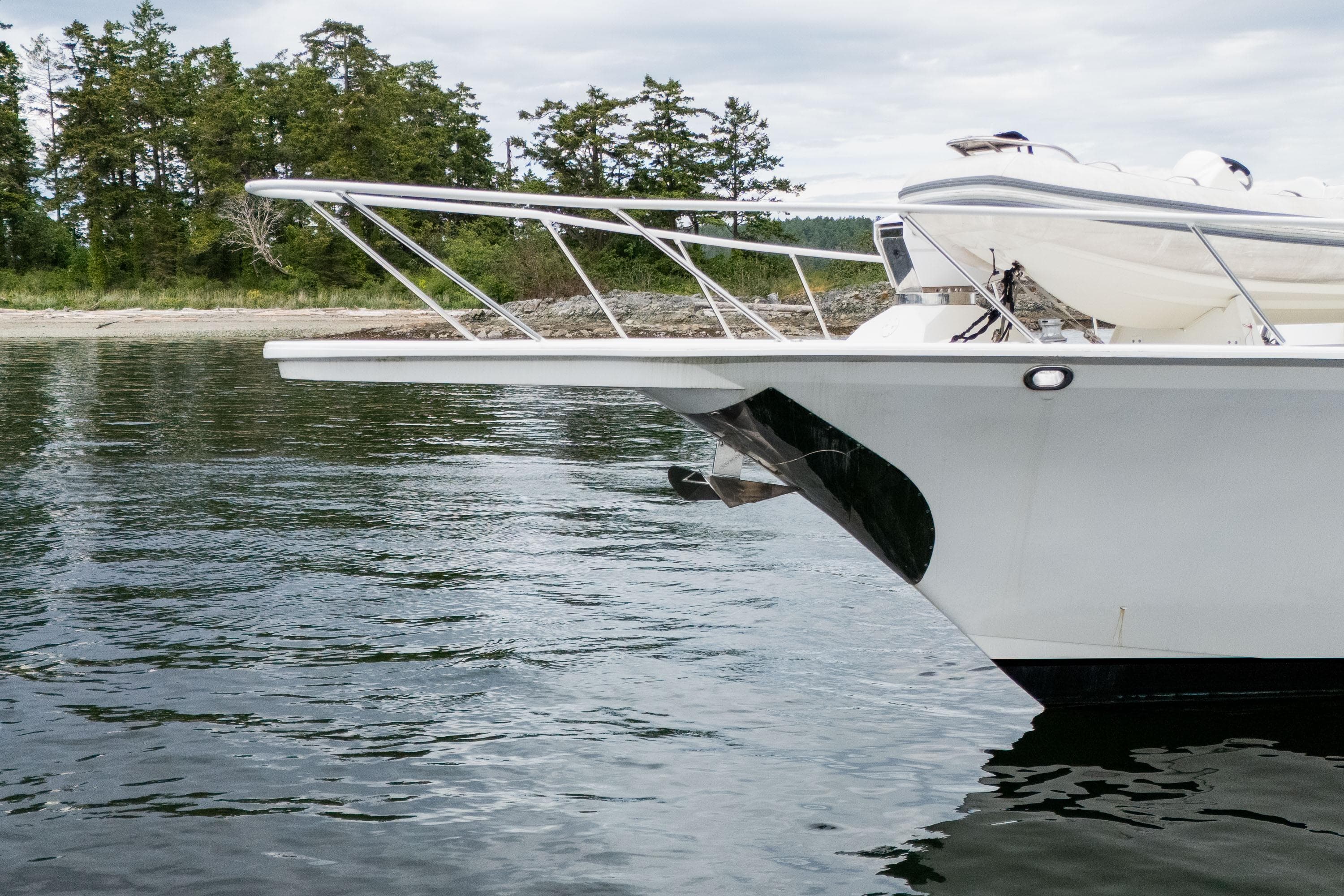 Bow of 2002 Striker 76 Sportfish Motor Yacht near a forested shoreline.