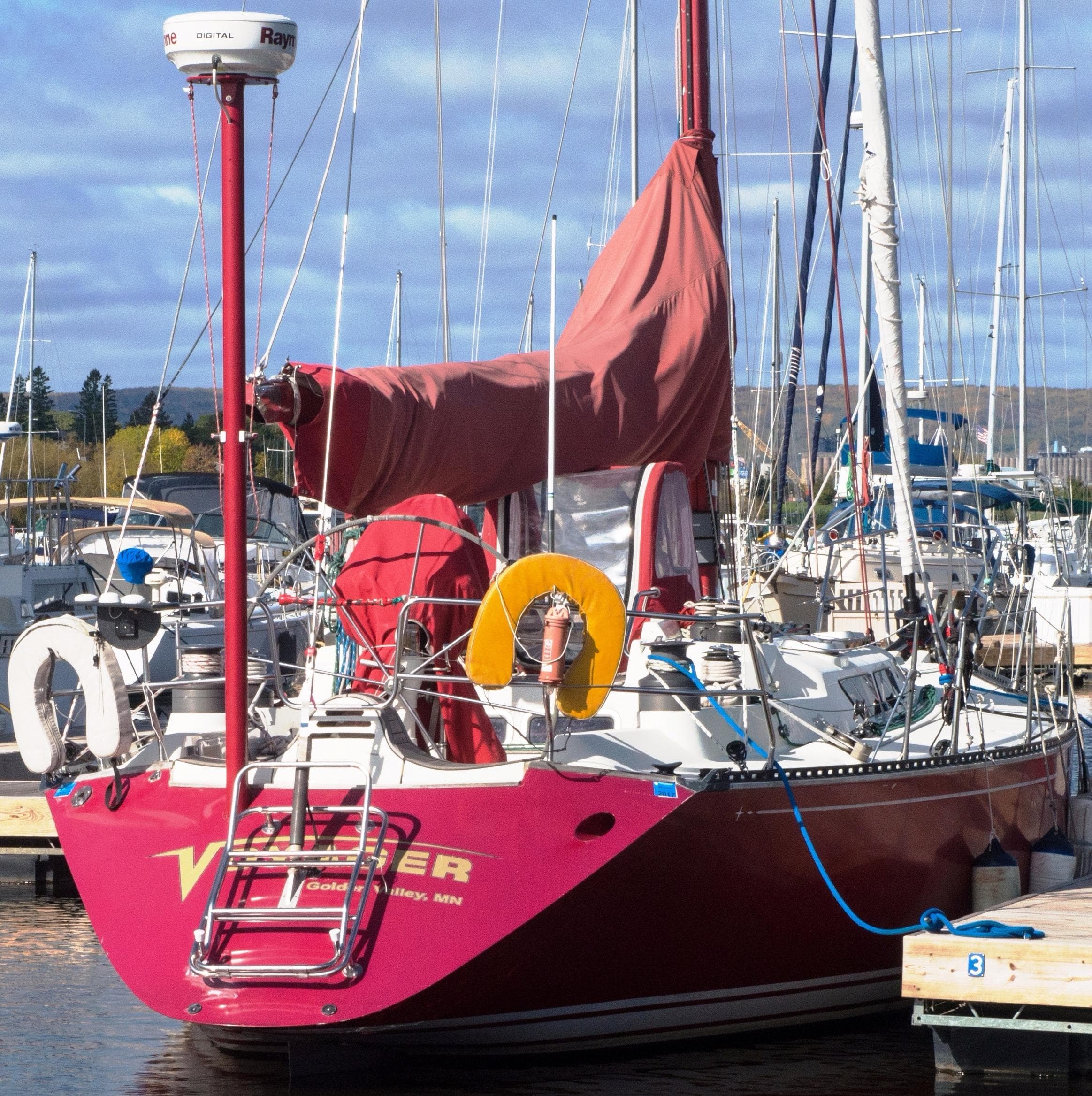Red 1985 C&C 44 sailboat docked at marina, featuring vibrant sails and nautical equipment.