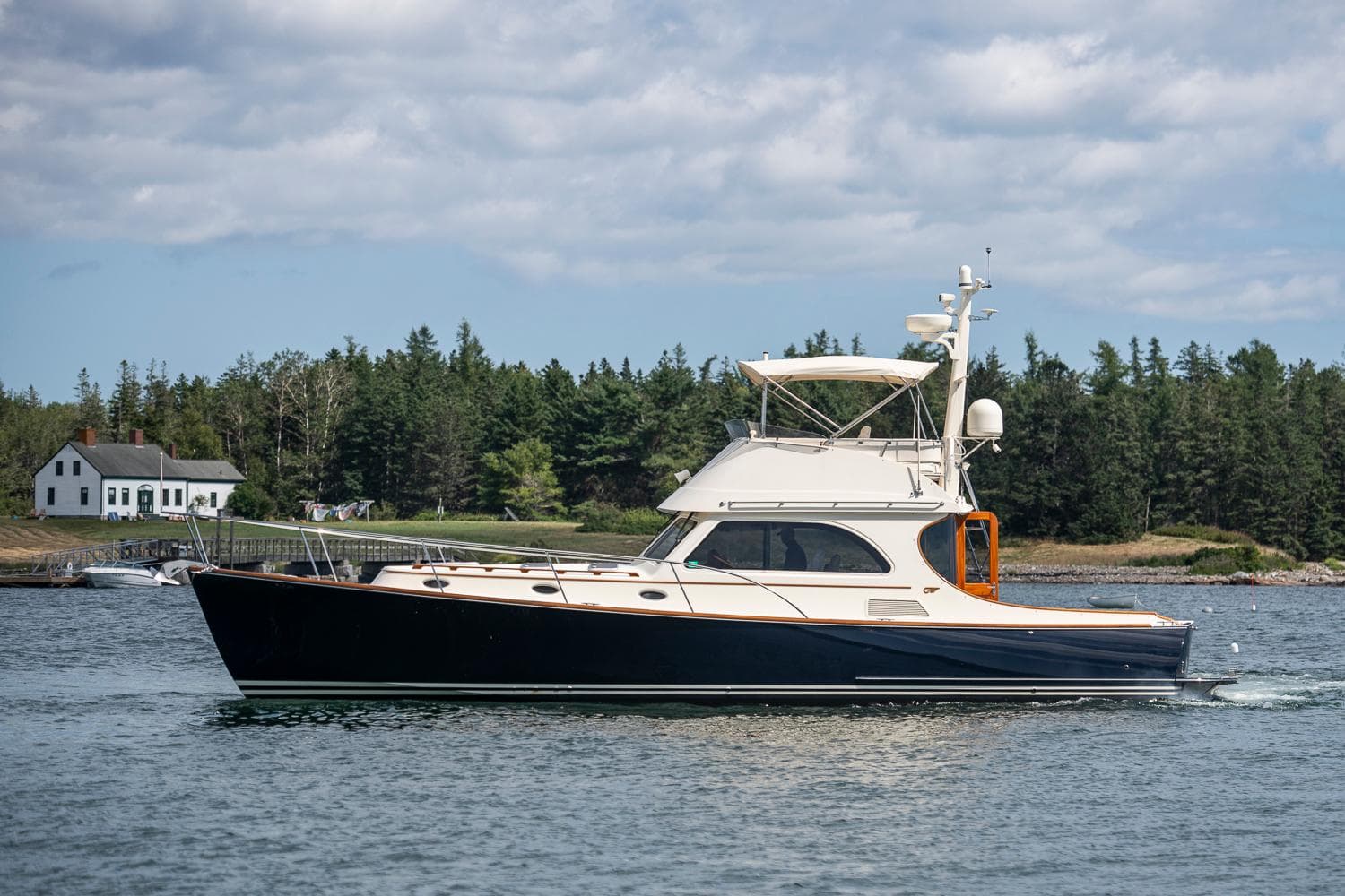 2006 Hinckley Talaria 44 FB yacht cruising on a serene lake with forested shoreline.