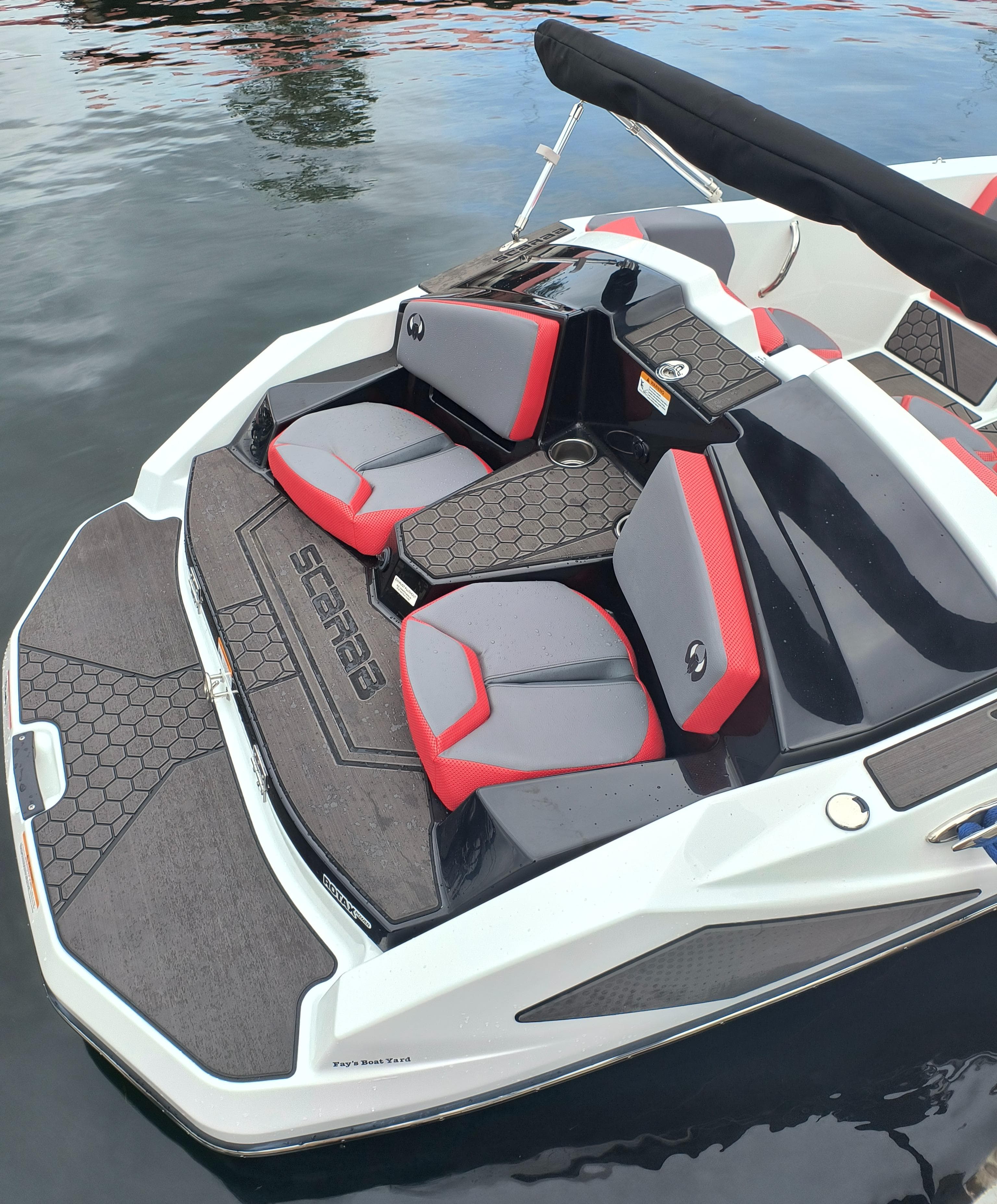 2025 Scarab 165 LX boat with red and gray seating, docked on calm water.