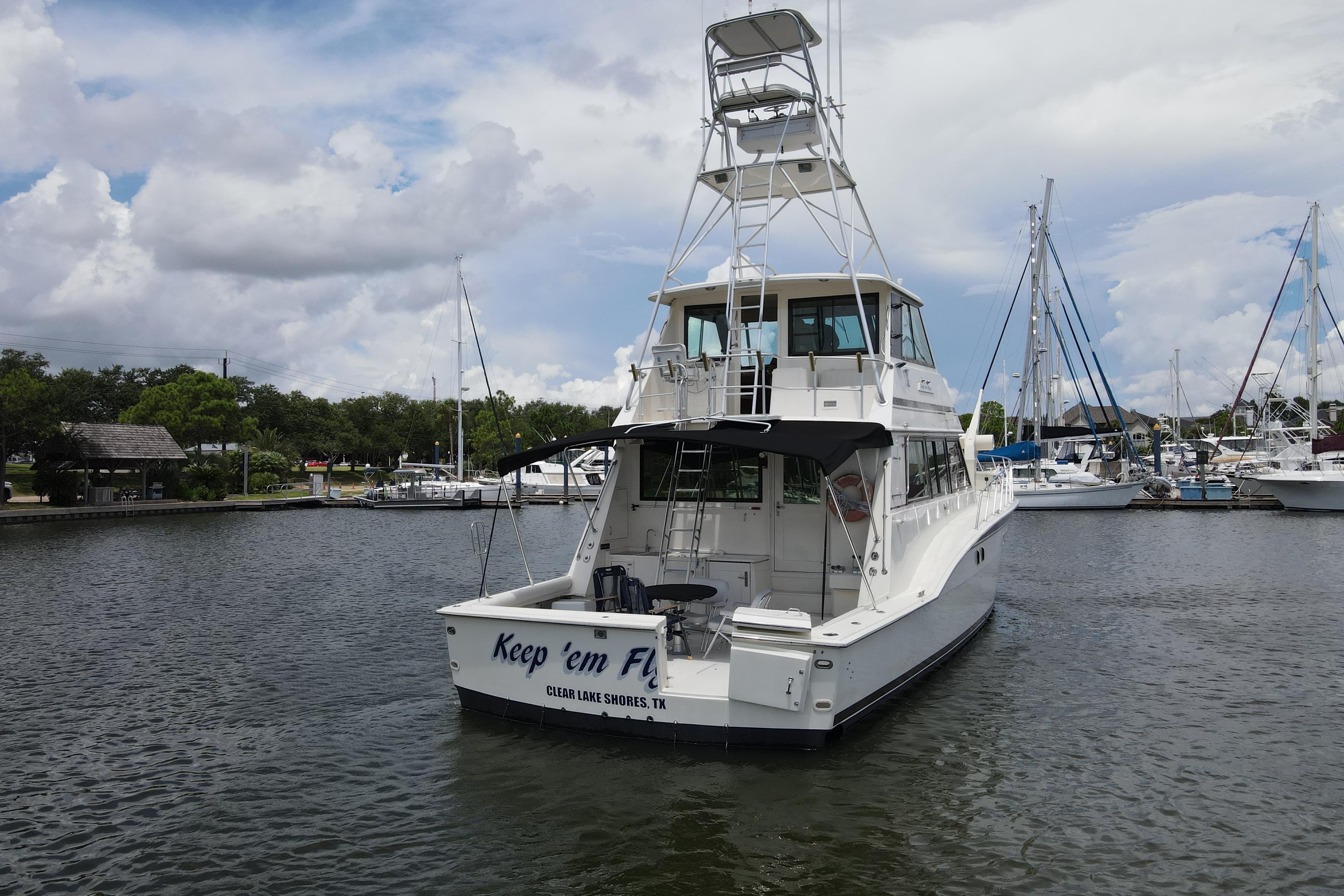 1985 Hatteras 60 Convertible yacht docked in a marina under a cloudy sky.