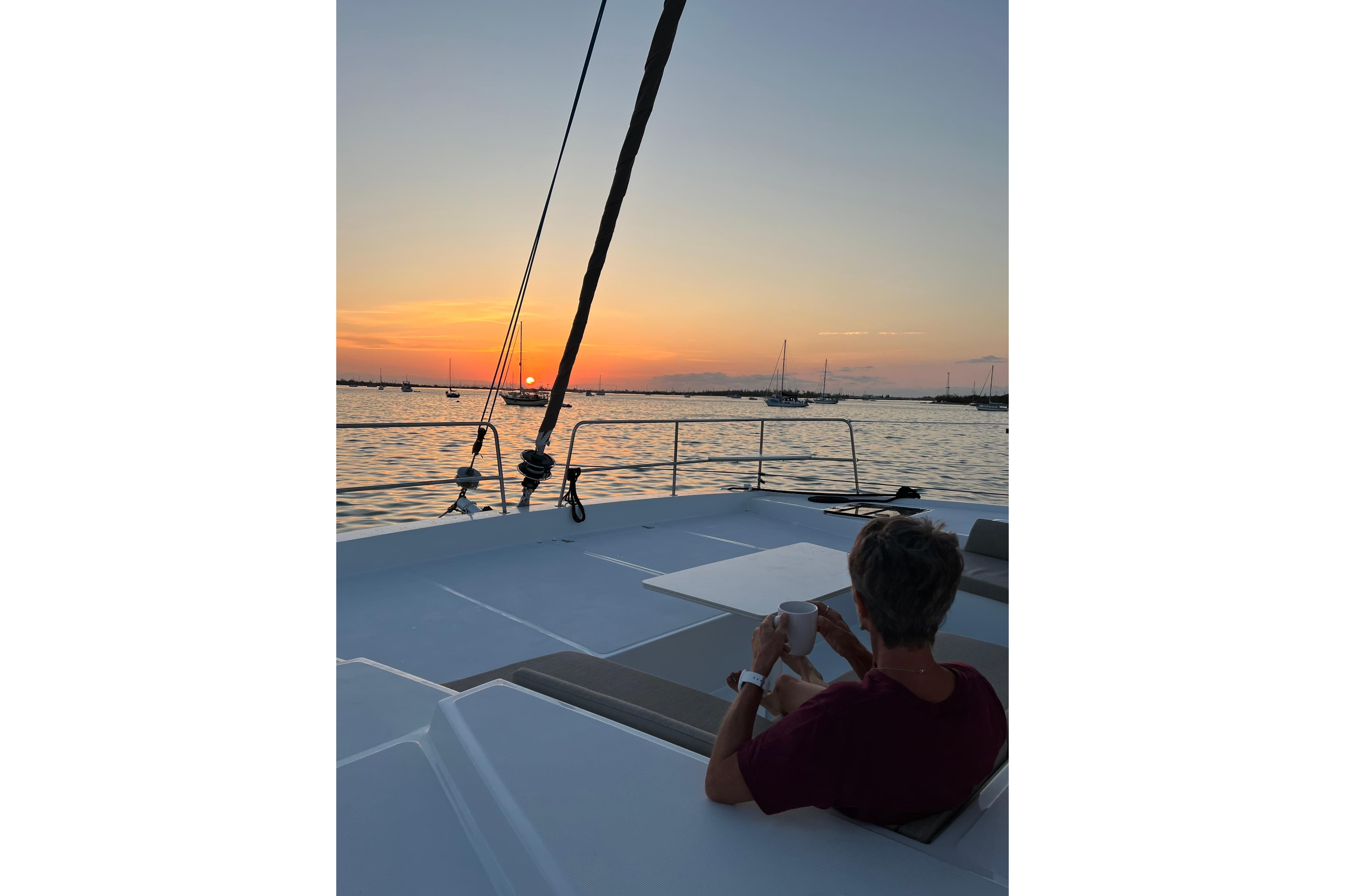 Person enjoying sunset on Bali 4.2 yacht, 2023 model, with a cup of coffee.