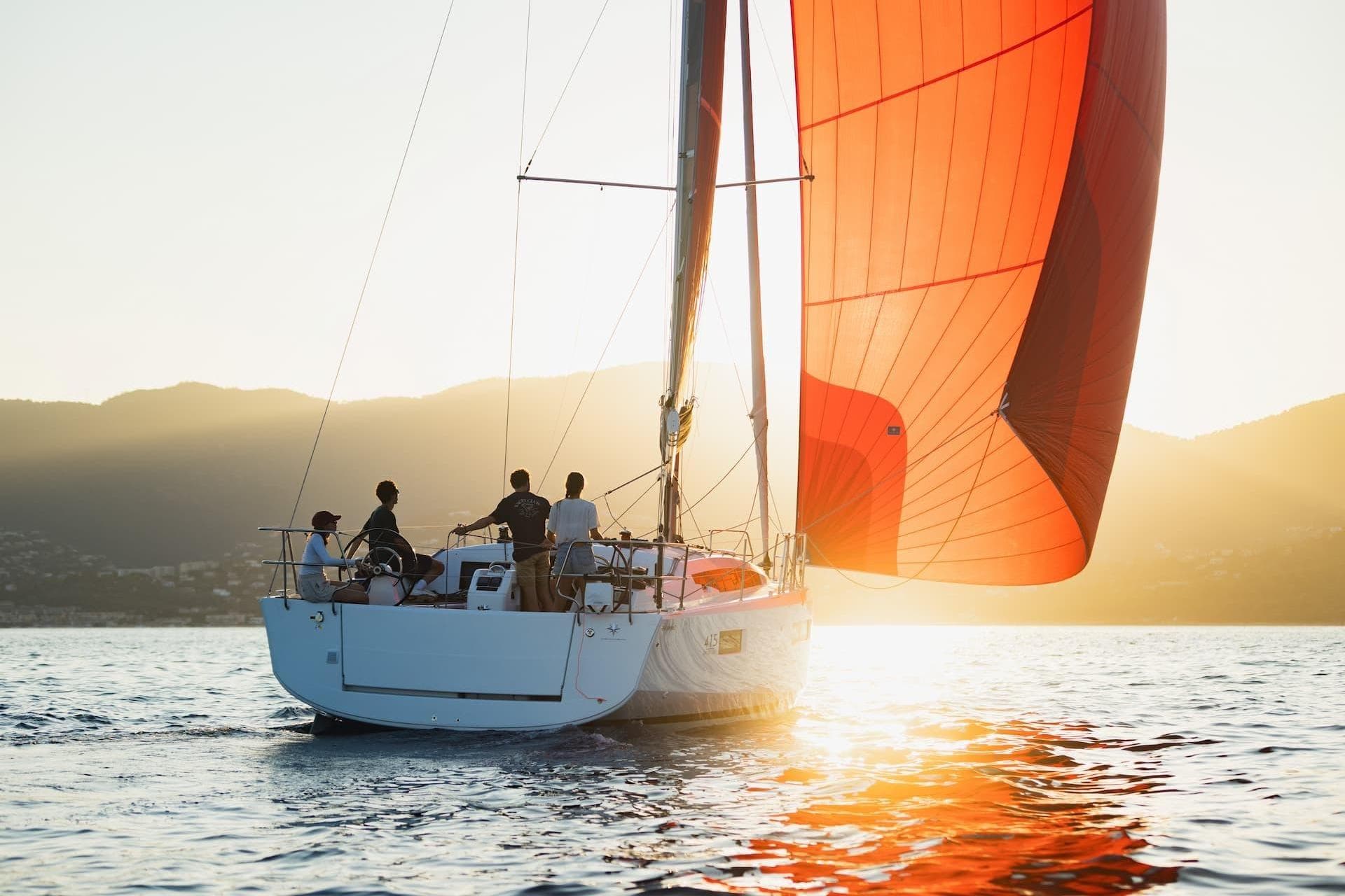 2026 Jeanneau Sun Odyssey 415 sailing at sunset with vibrant red sails.
