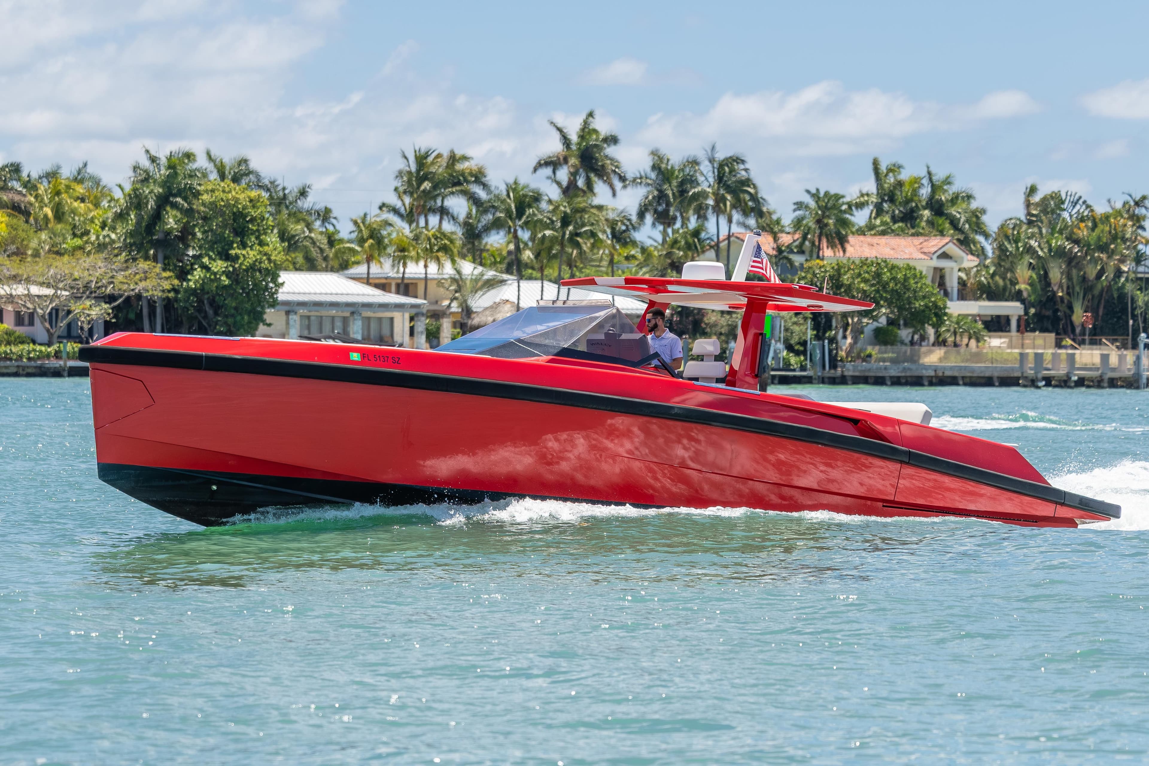 Red 2021 Wally 48 yacht cruising on a sunny day near waterfront homes.