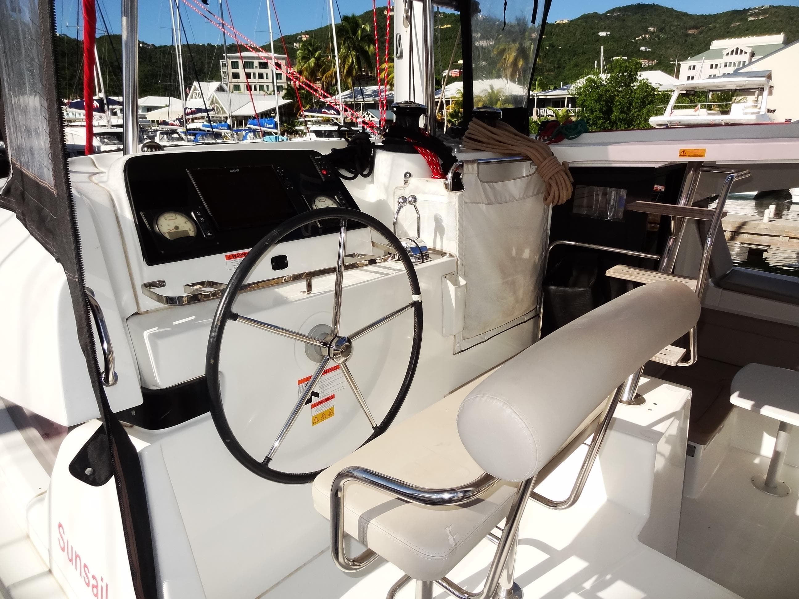 Lagoon 42 catamaran helm station, 2020 model, docked at a marina with scenic background.