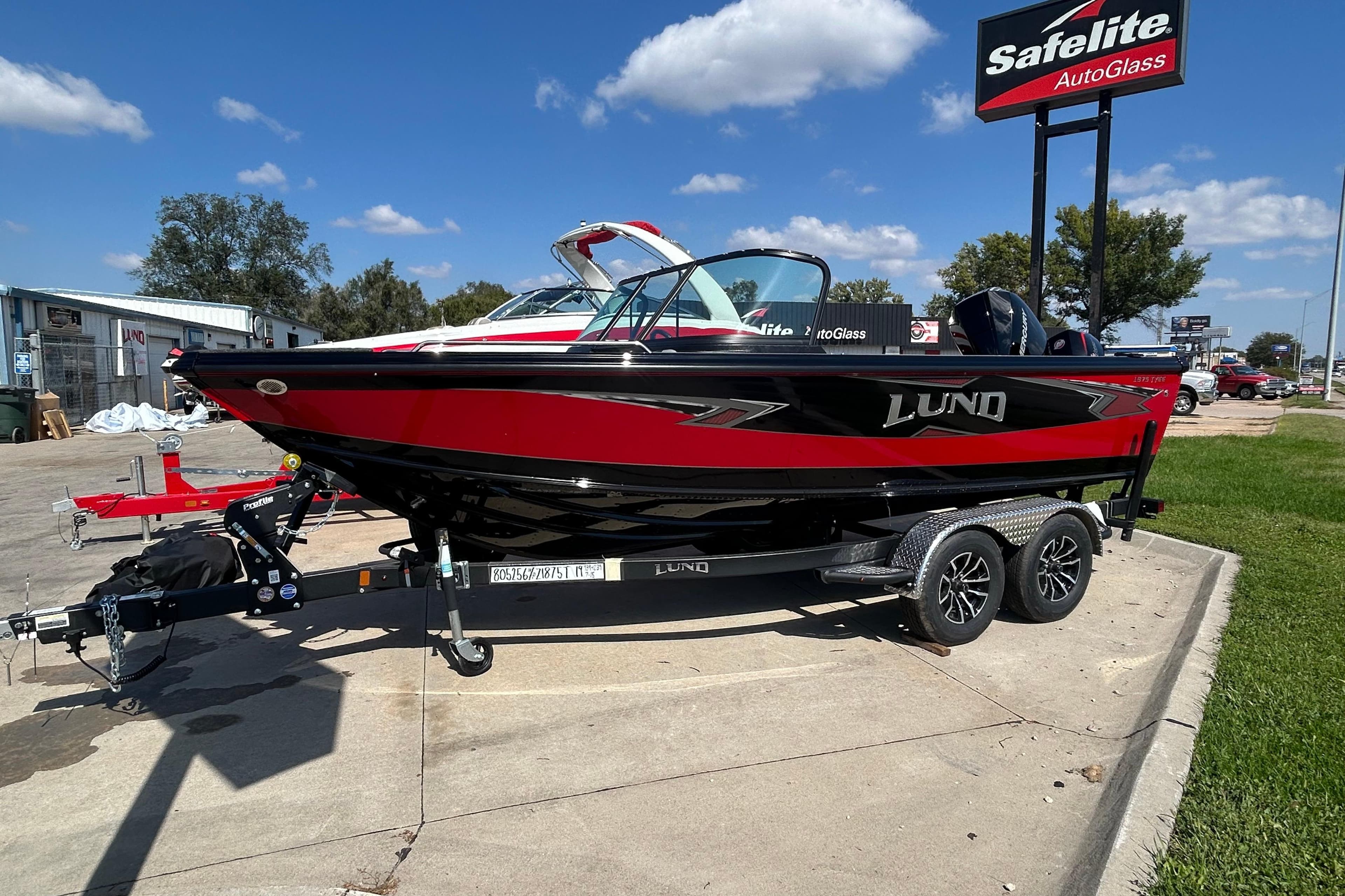 2026 Lund 1875 Tyee boat in red and black on a trailer, parked outdoors.