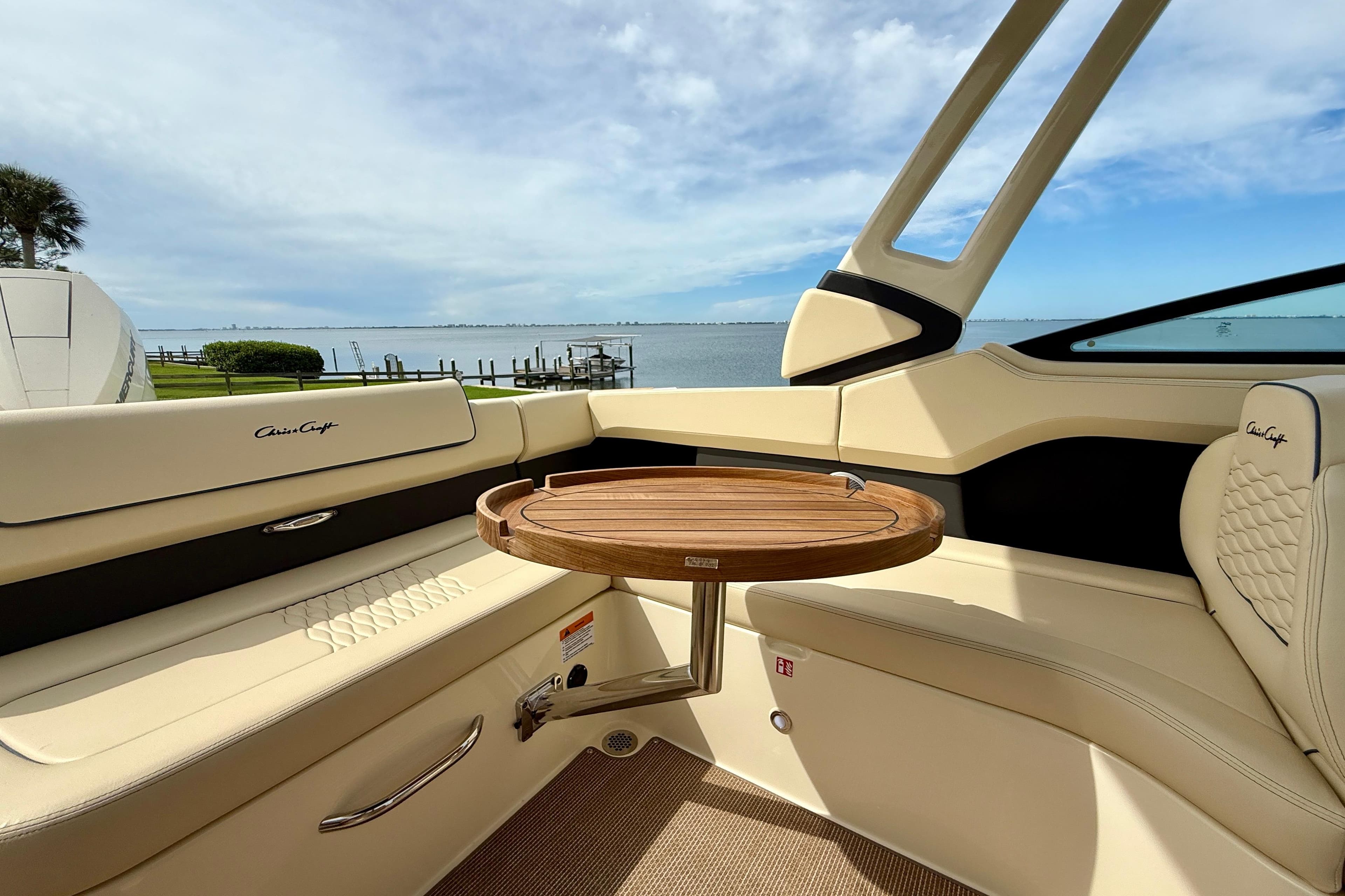 2026 Chris-Craft Sportster 28 interior with elegant seating and wooden table, overlooking serene waters.
