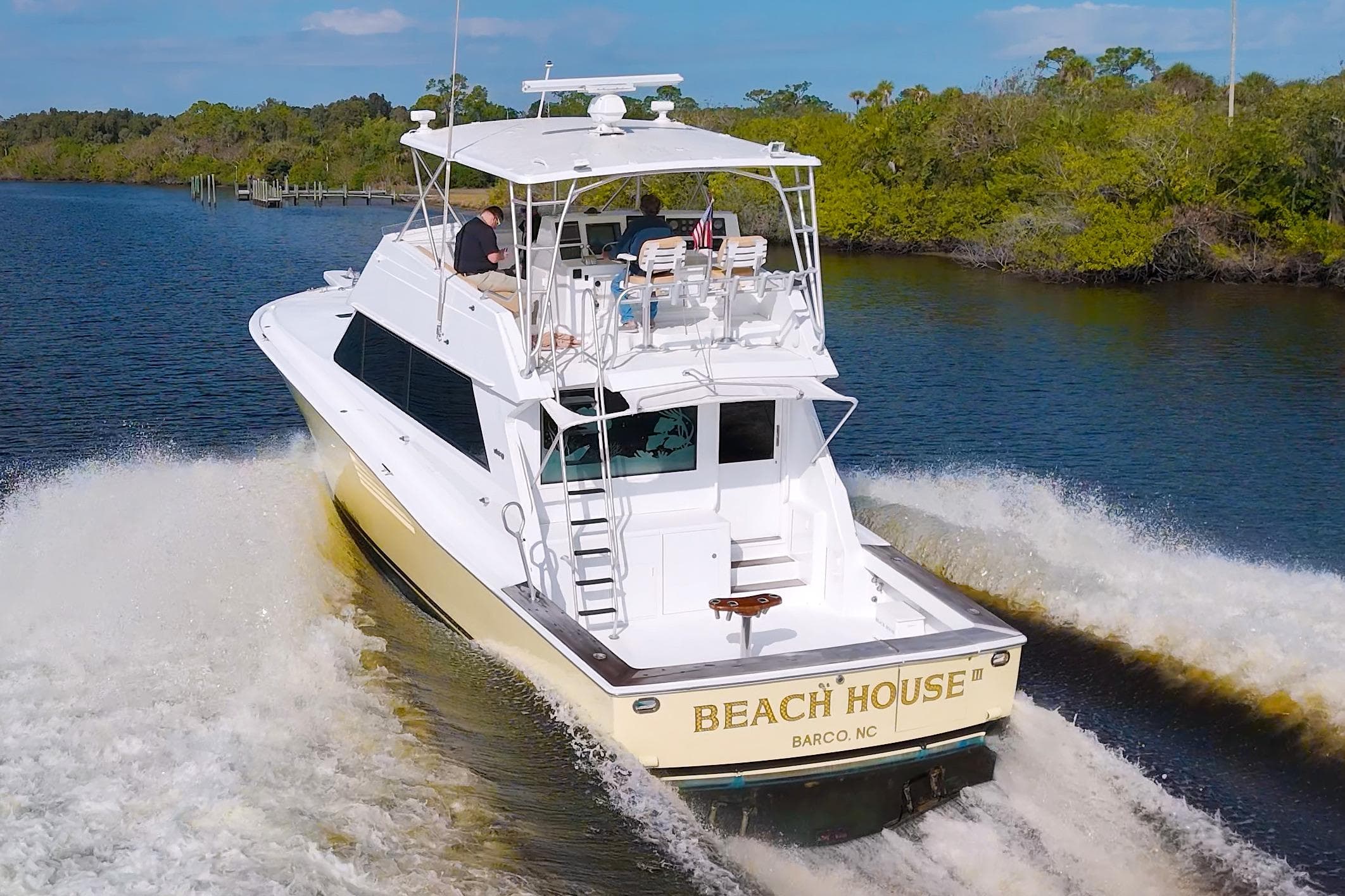 1990 Viking 53 Convertible yacht cruising on a river, named "Beach House," with lush greenery.