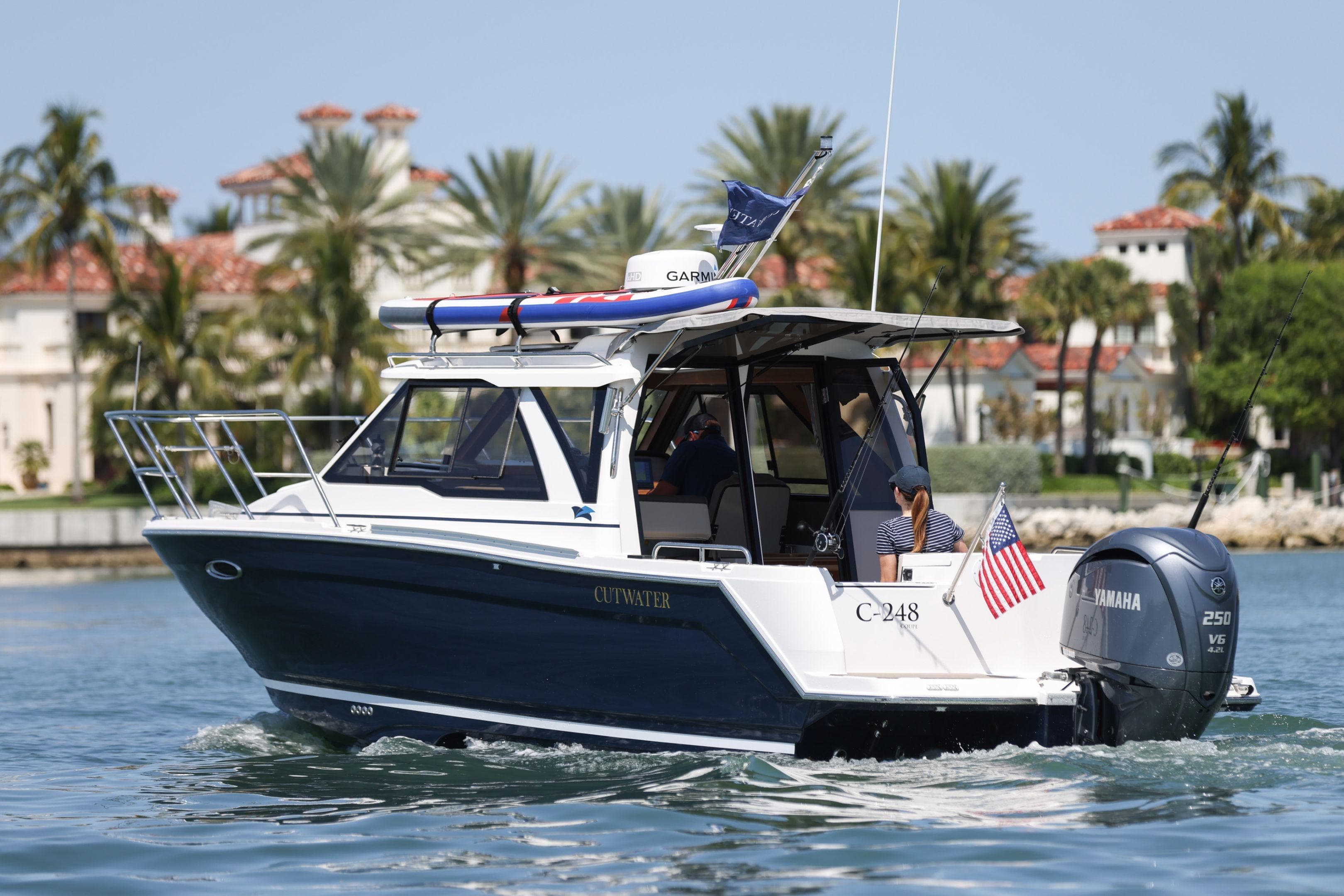 2026 Cutwater C-248 Coupe boat cruising near palm-lined waterfront homes.