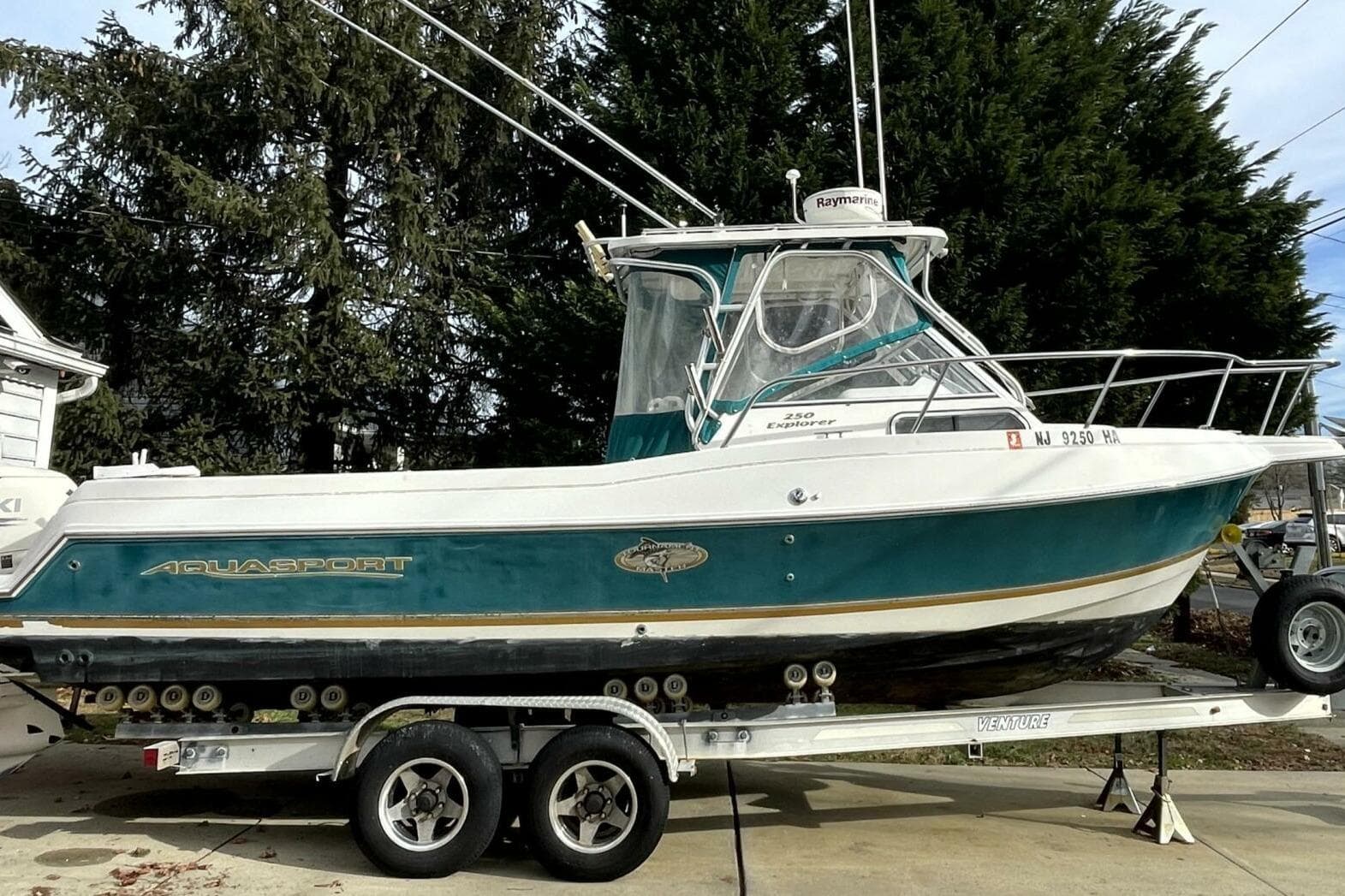 2001 Aquasport 250 Explorer boat on trailer, parked outdoors with trees in background.
