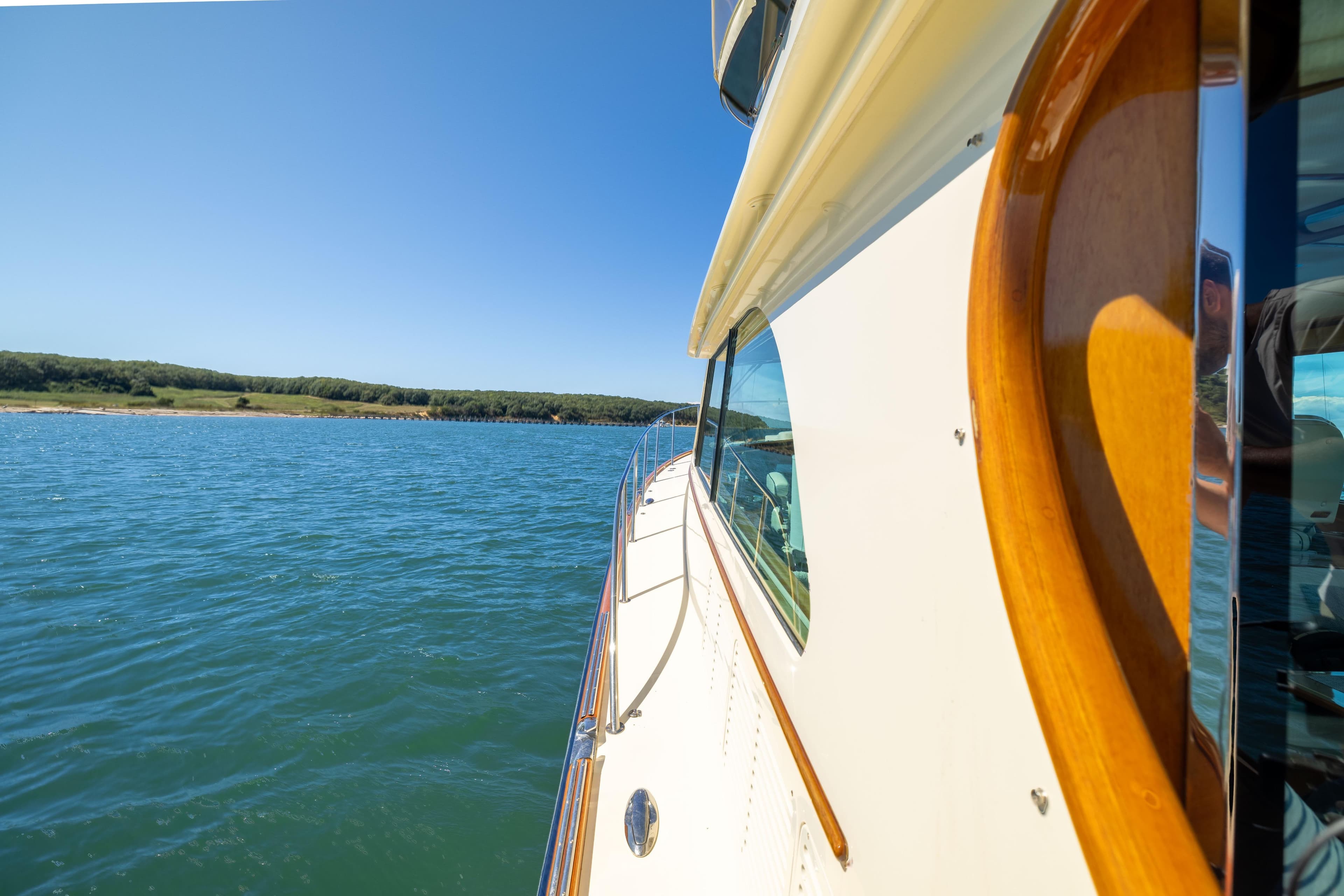 2014 Hinckley Talaria 48 Flybridge cruising on a sunny day, near a scenic shoreline.