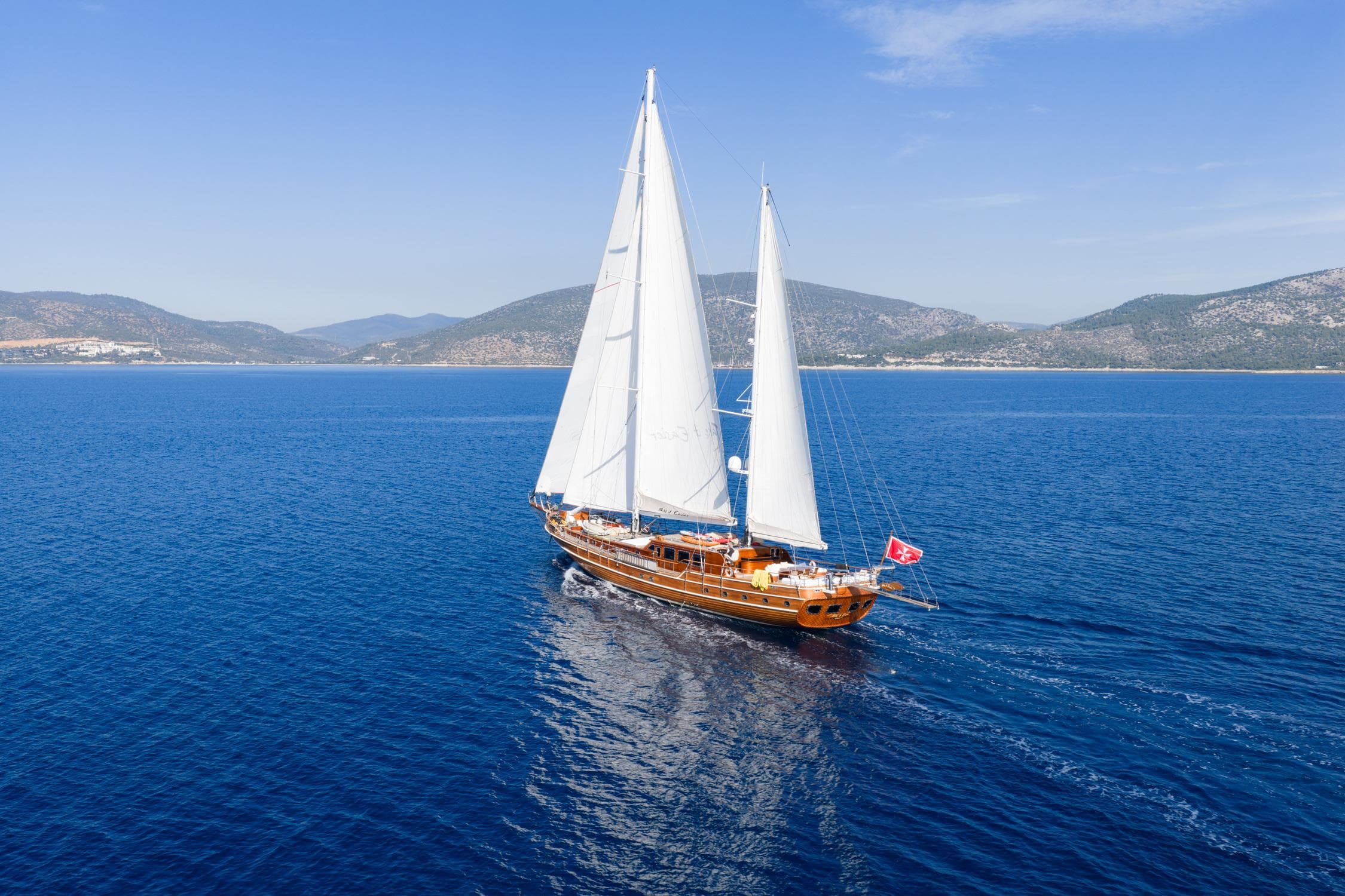 Custom 2007 Gulet Motorsailer sailing on blue sea with scenic coastal backdrop.
