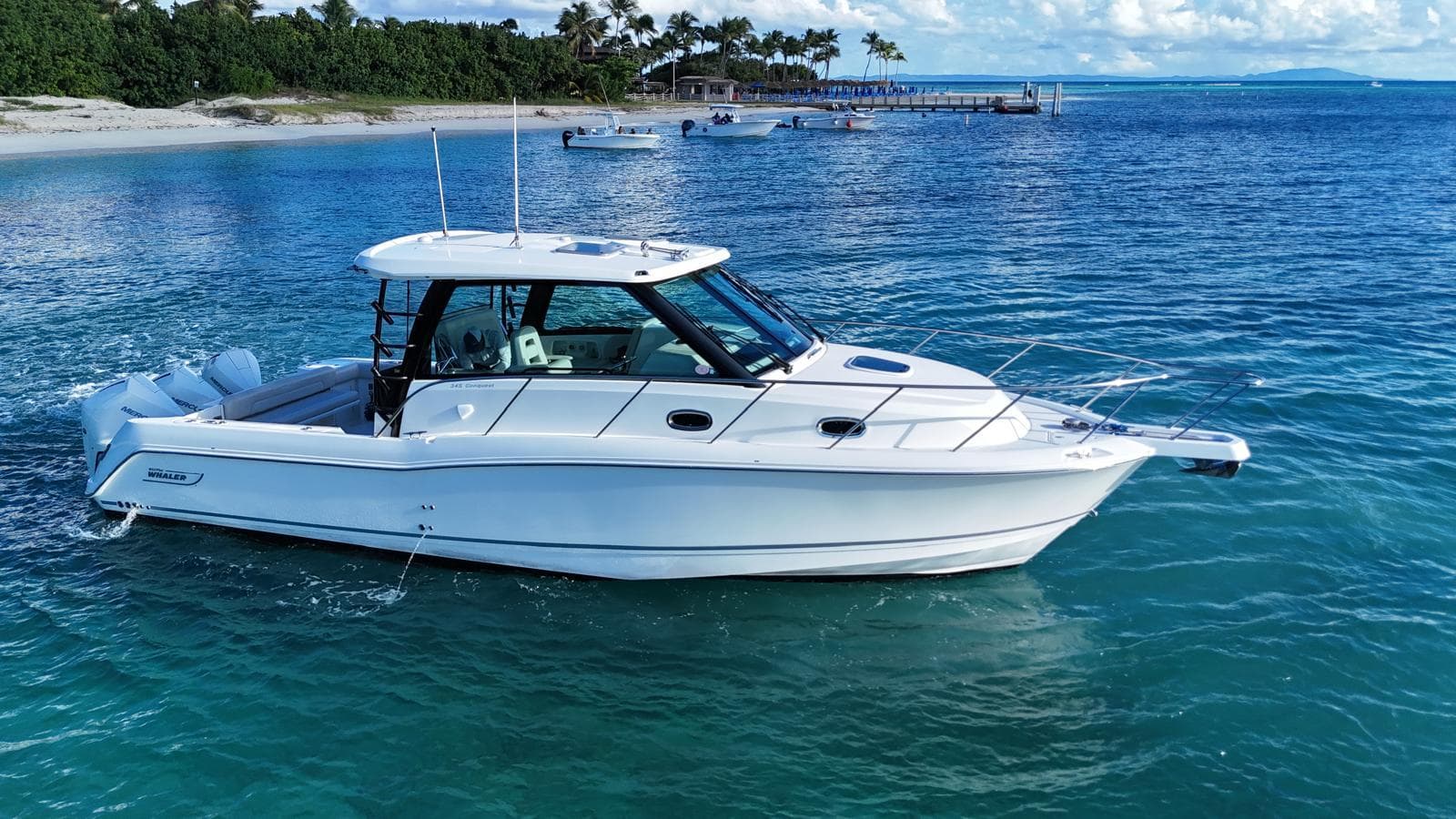 2022 Boston Whaler 345 Conquest cruising in clear blue waters near a tropical beach.