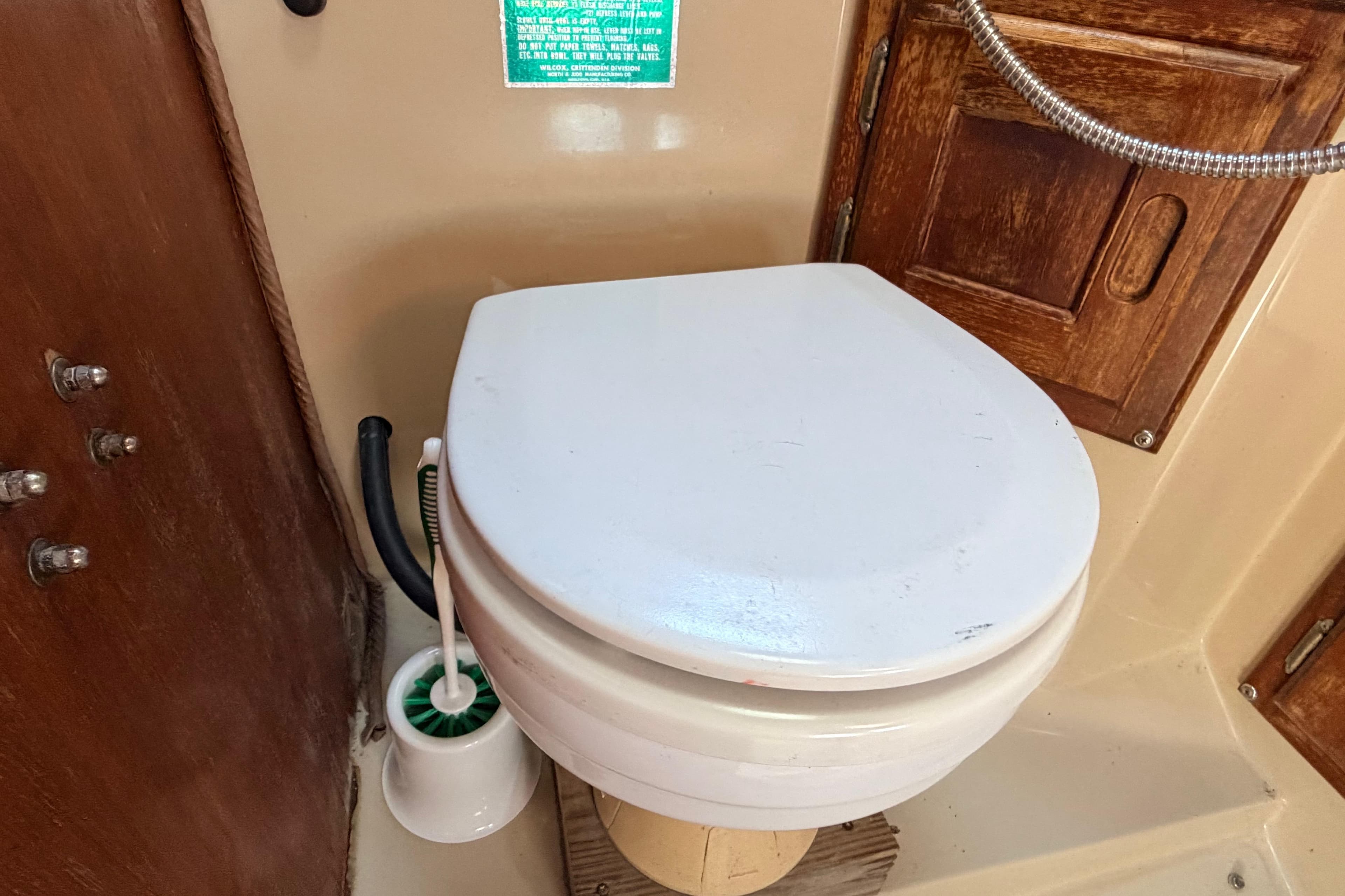 Boat bathroom with white toilet, wooden paneling, and cleaning brush on a 1981 Catalina 30.