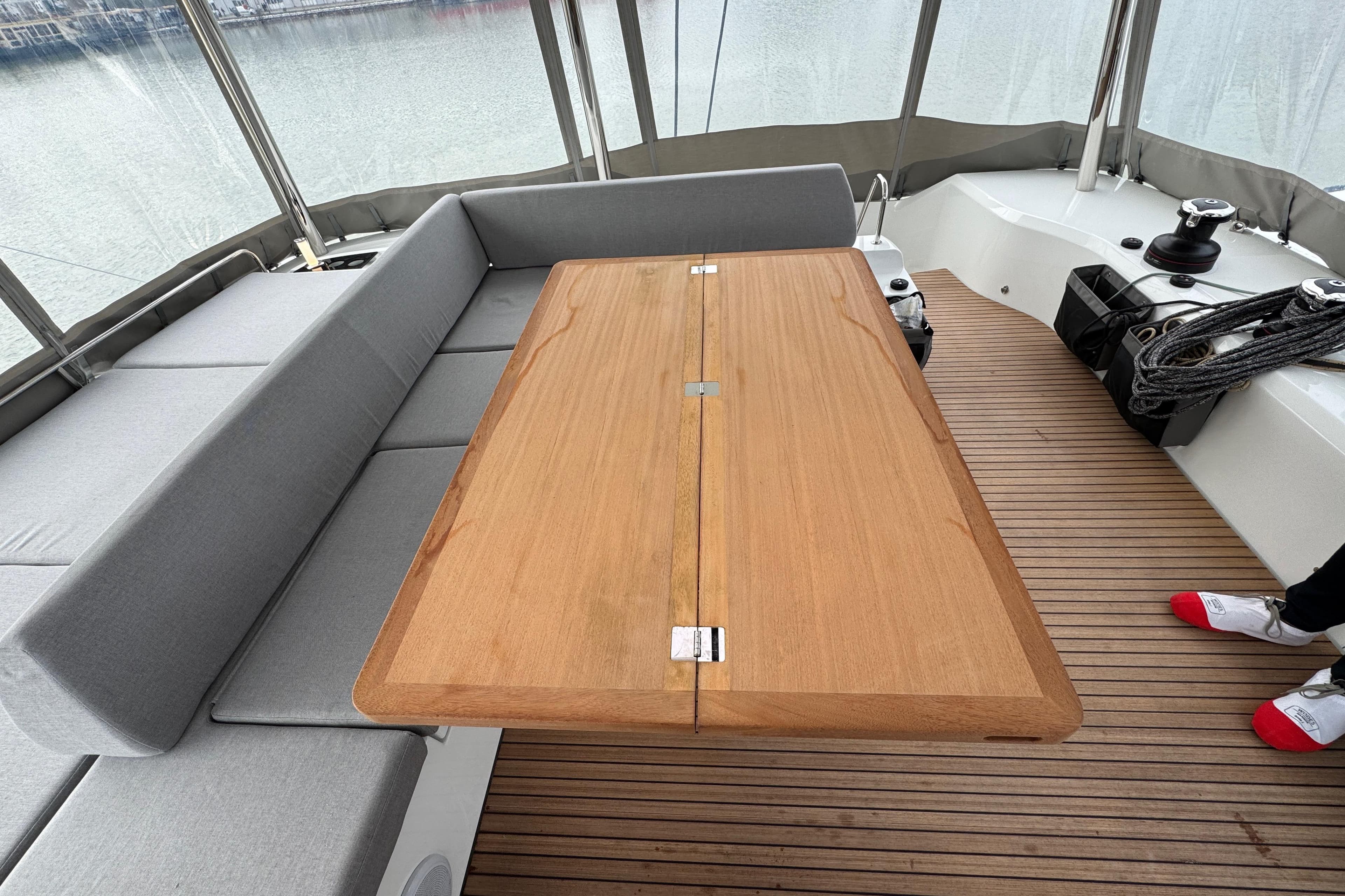 Spacious deck seating on 2026 Lagoon 55 yacht with wooden table and gray cushions.