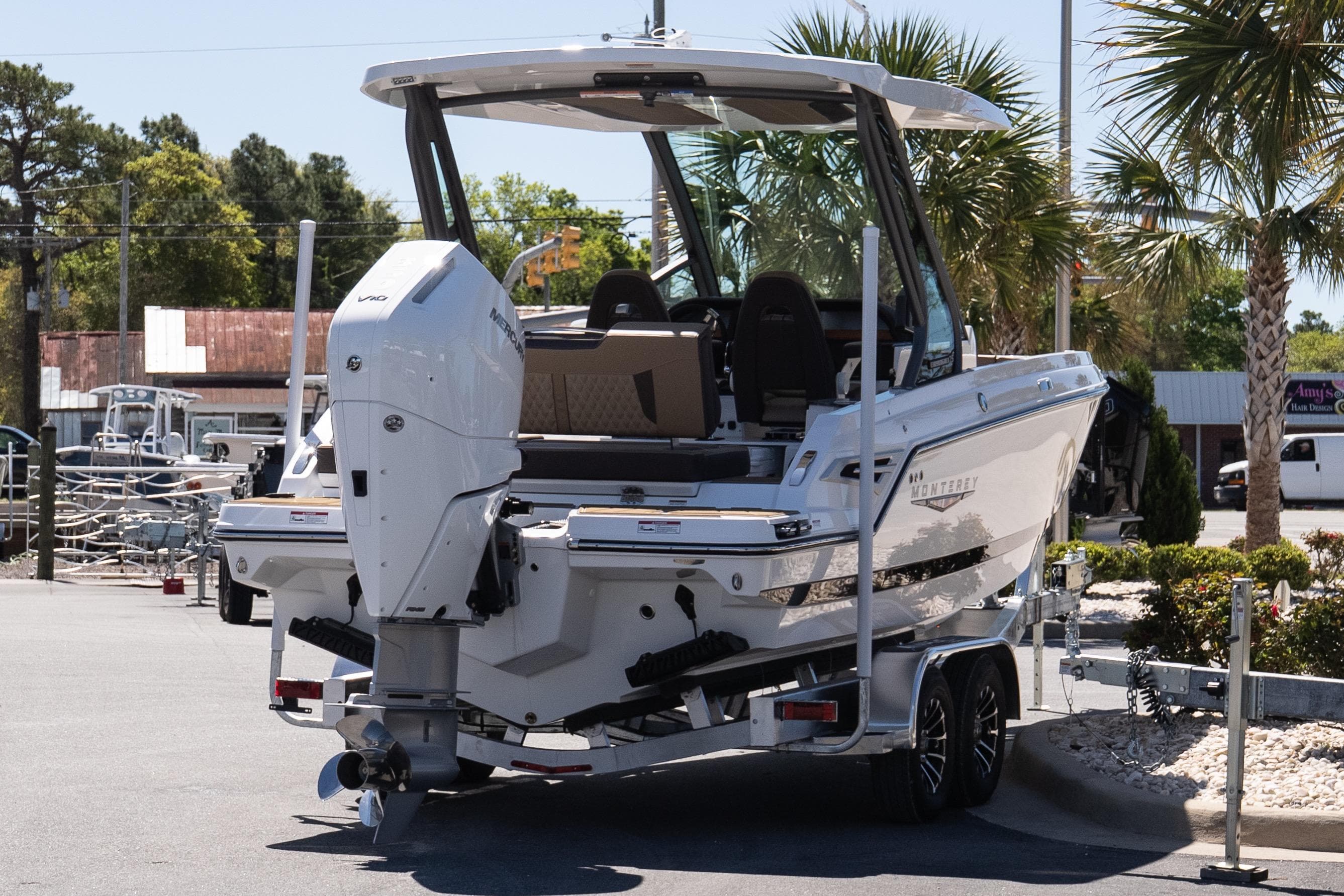 2026 Monterey Elite 25 OB boat on trailer, parked outdoors with palm trees in background.