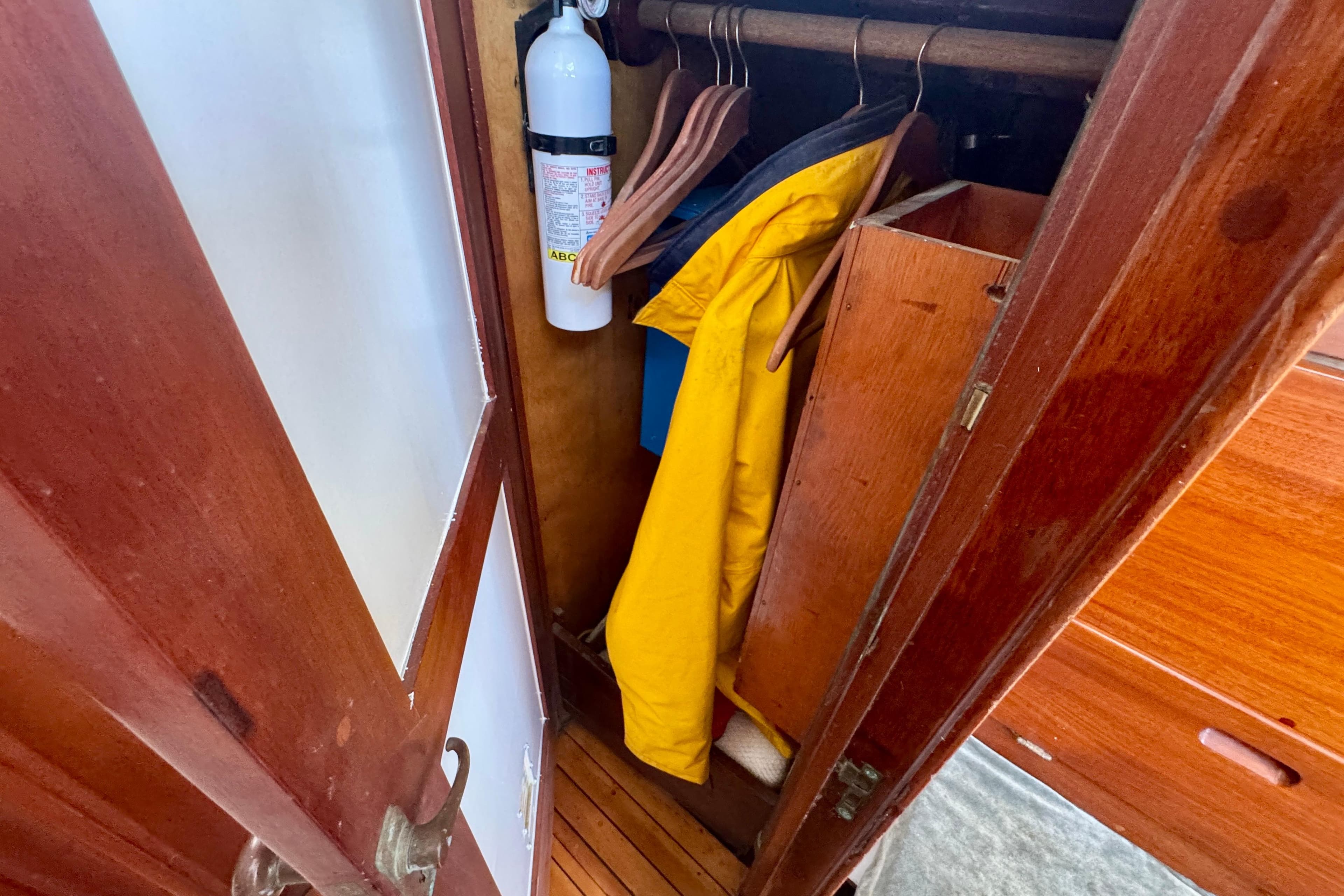 Wooden closet on a 1946 Phillip Rhodes 42 boat, featuring a yellow jacket and fire extinguisher.