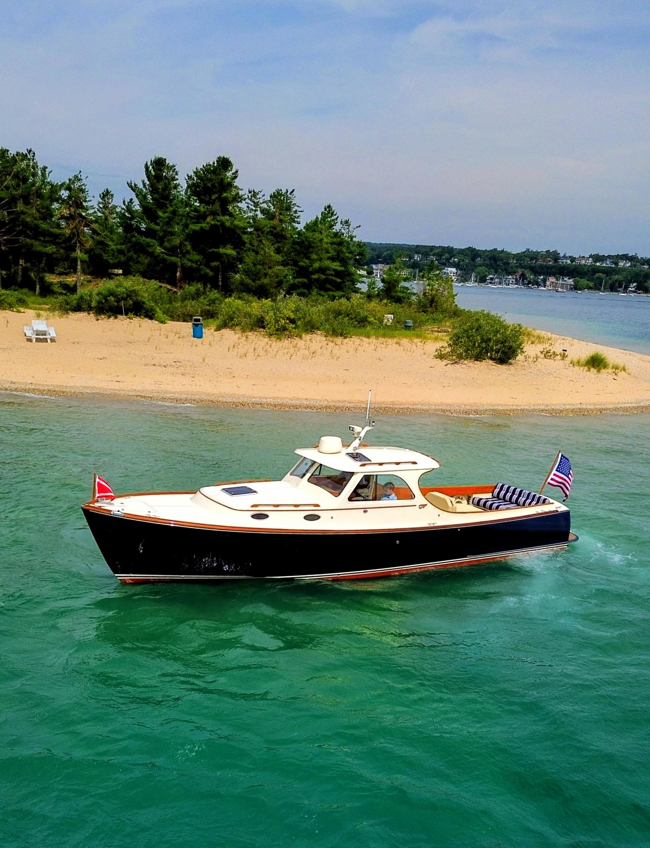 Hinckley Picnic Boat 2000 cruising near a sandy beach with lush greenery.