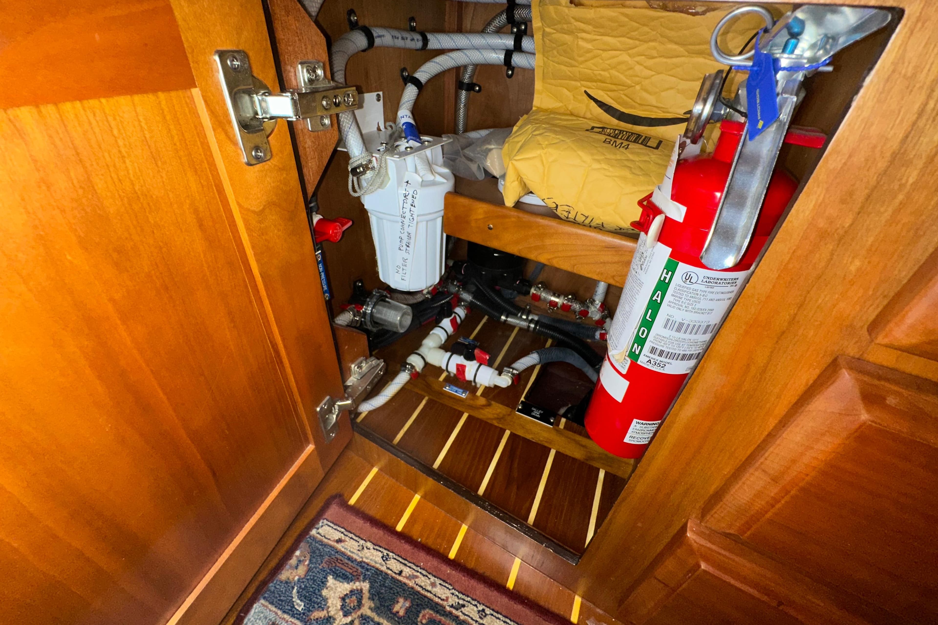Wooden cabinet interior with fire extinguisher and plumbing components on a 2007 Sabre 386.