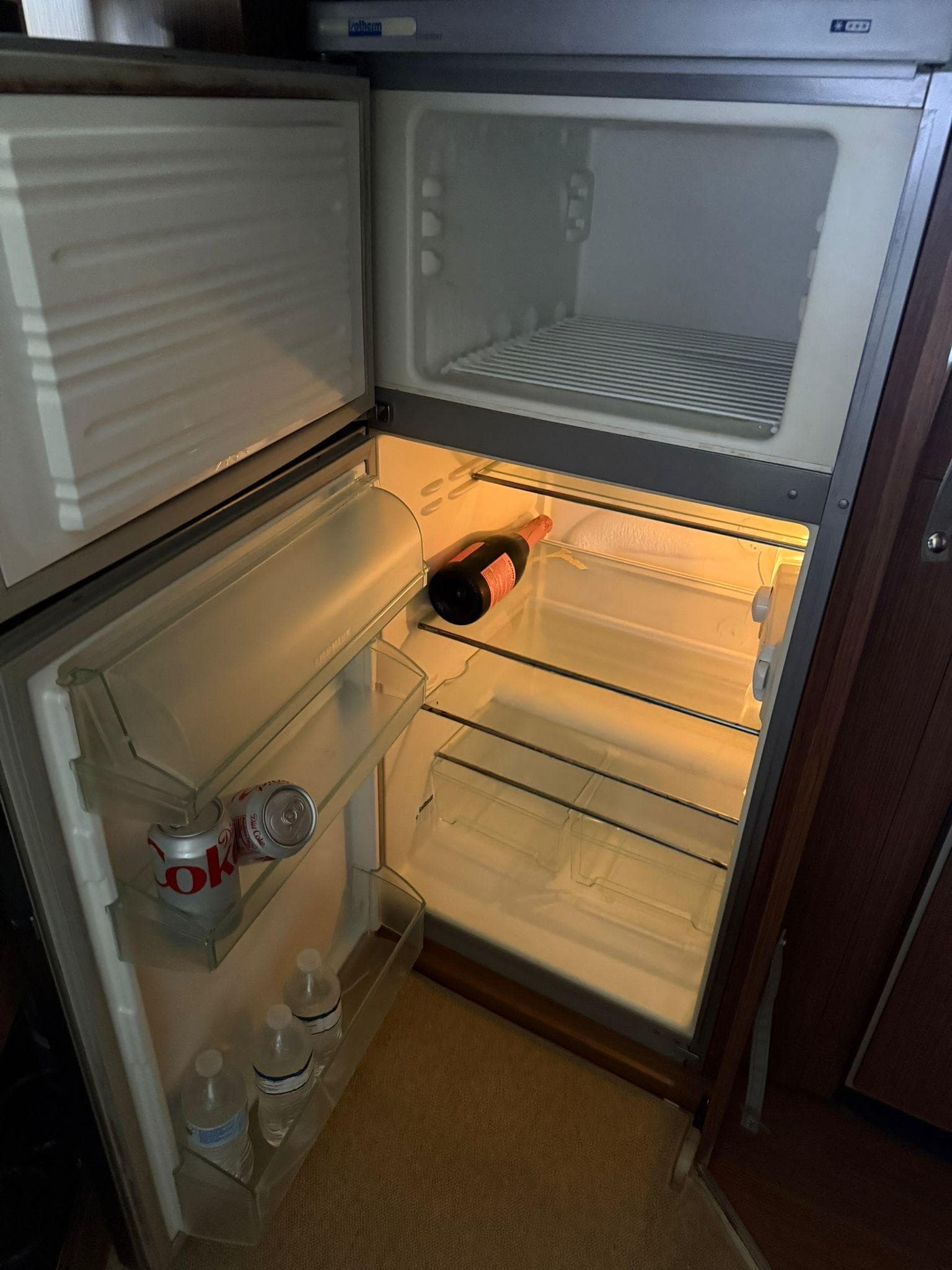 Open fridge in a 2012 Riva Rivale, containing drinks and a wine bottle.