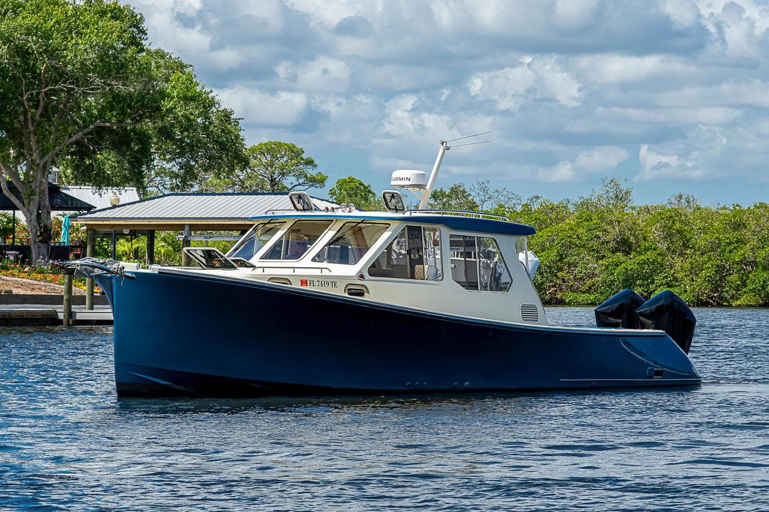 2002 True North 38 boat on water, surrounded by lush greenery and a cloudy sky.