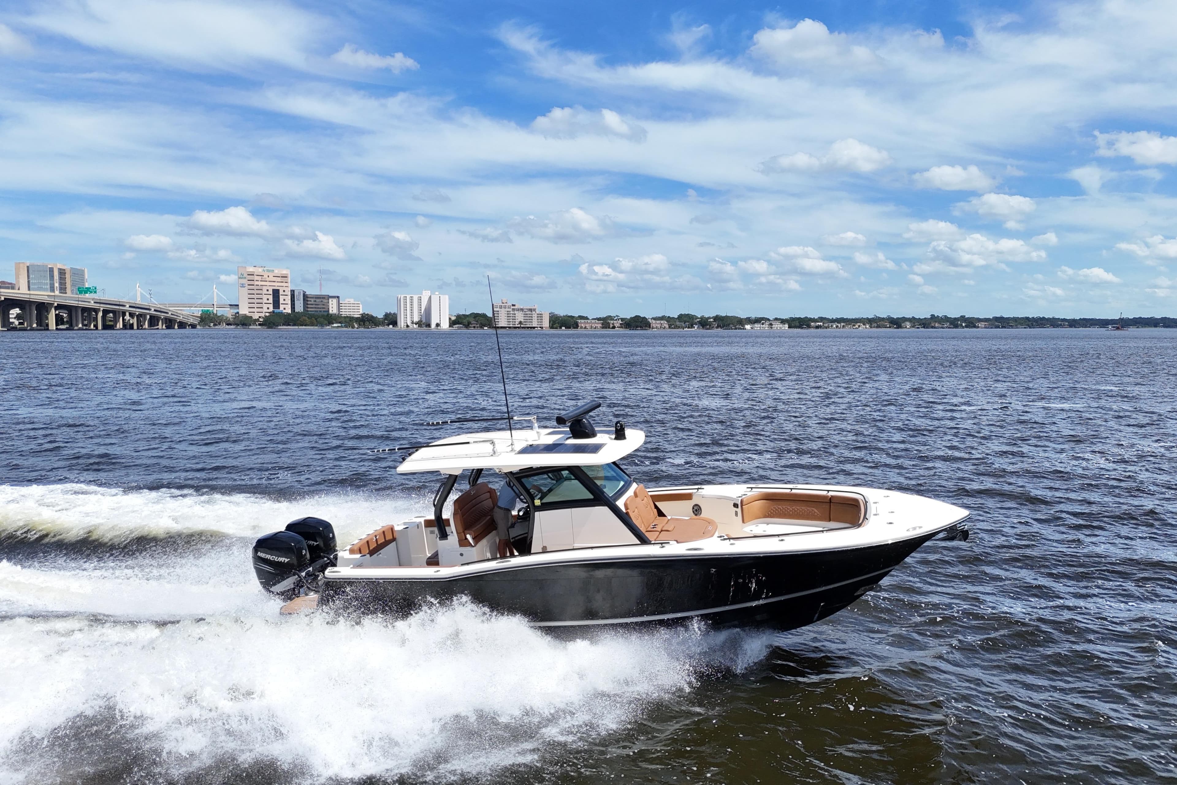 2021 Scout 330 LXF boat cruising on a sunny day with cityscape background.