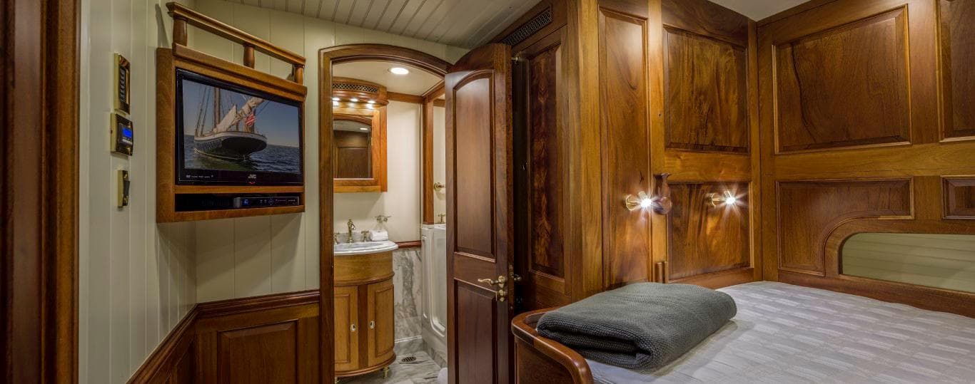 Luxurious wooden cabin interior on 2014 Eastern Shipbuilding Schooner, featuring bed, TV, and ensuite bathroom.