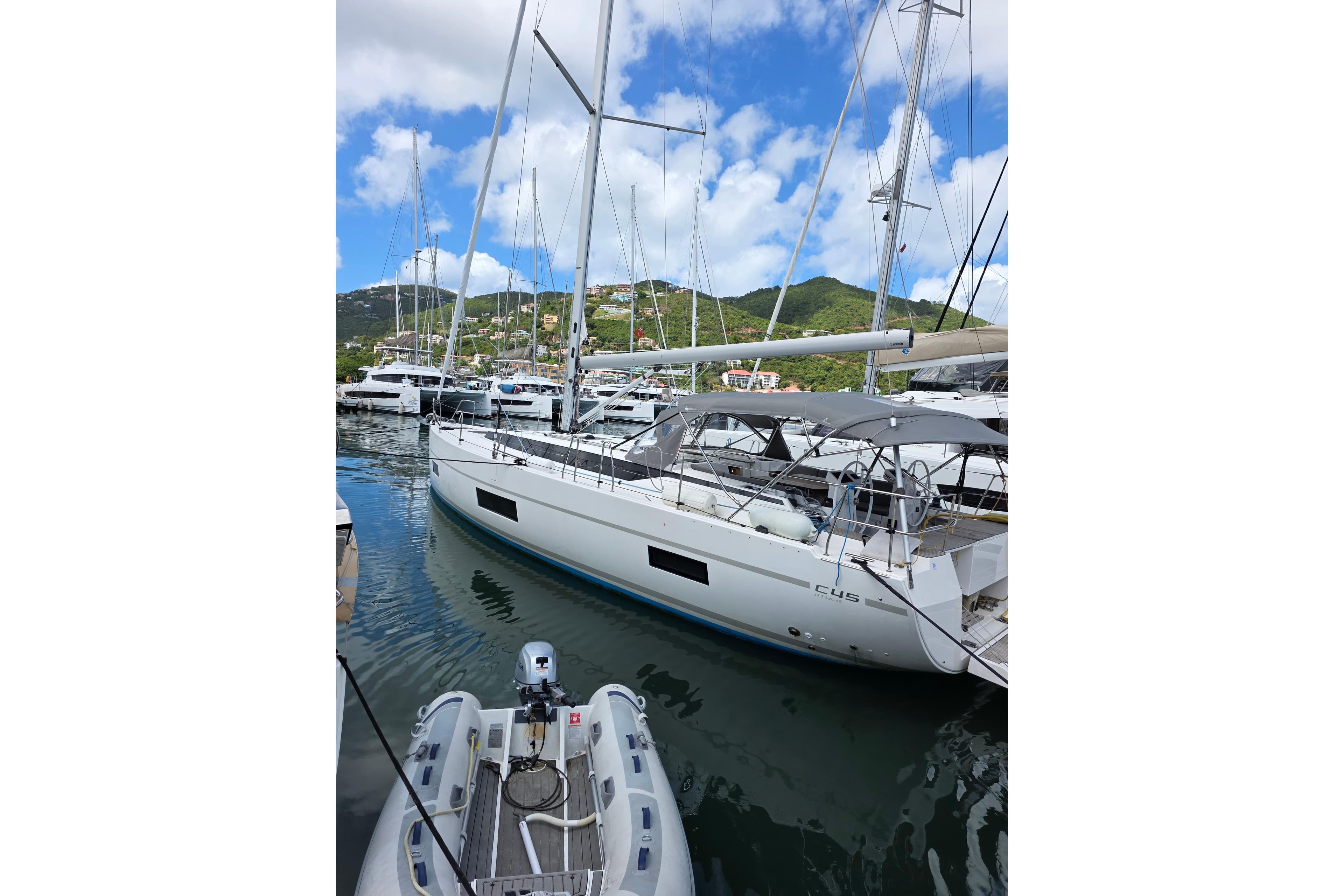 2023 Bavaria C45 yacht docked in a marina with scenic hillside backdrop.