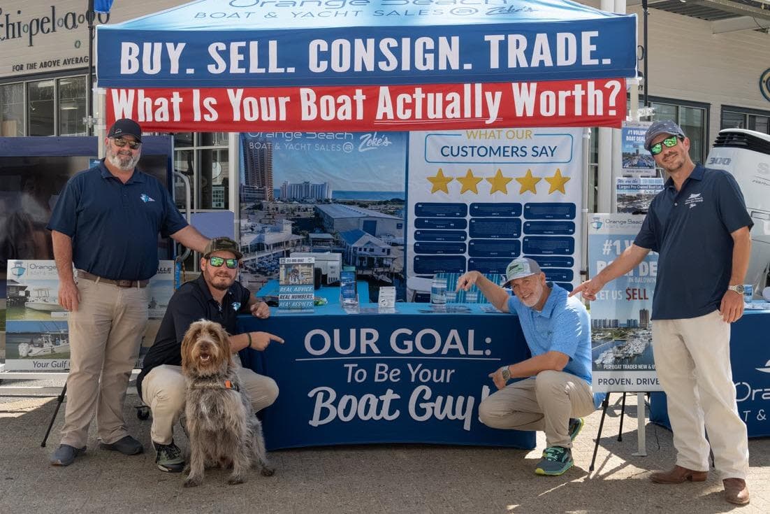 Group at boat sales booth with promotional banners and a dog.