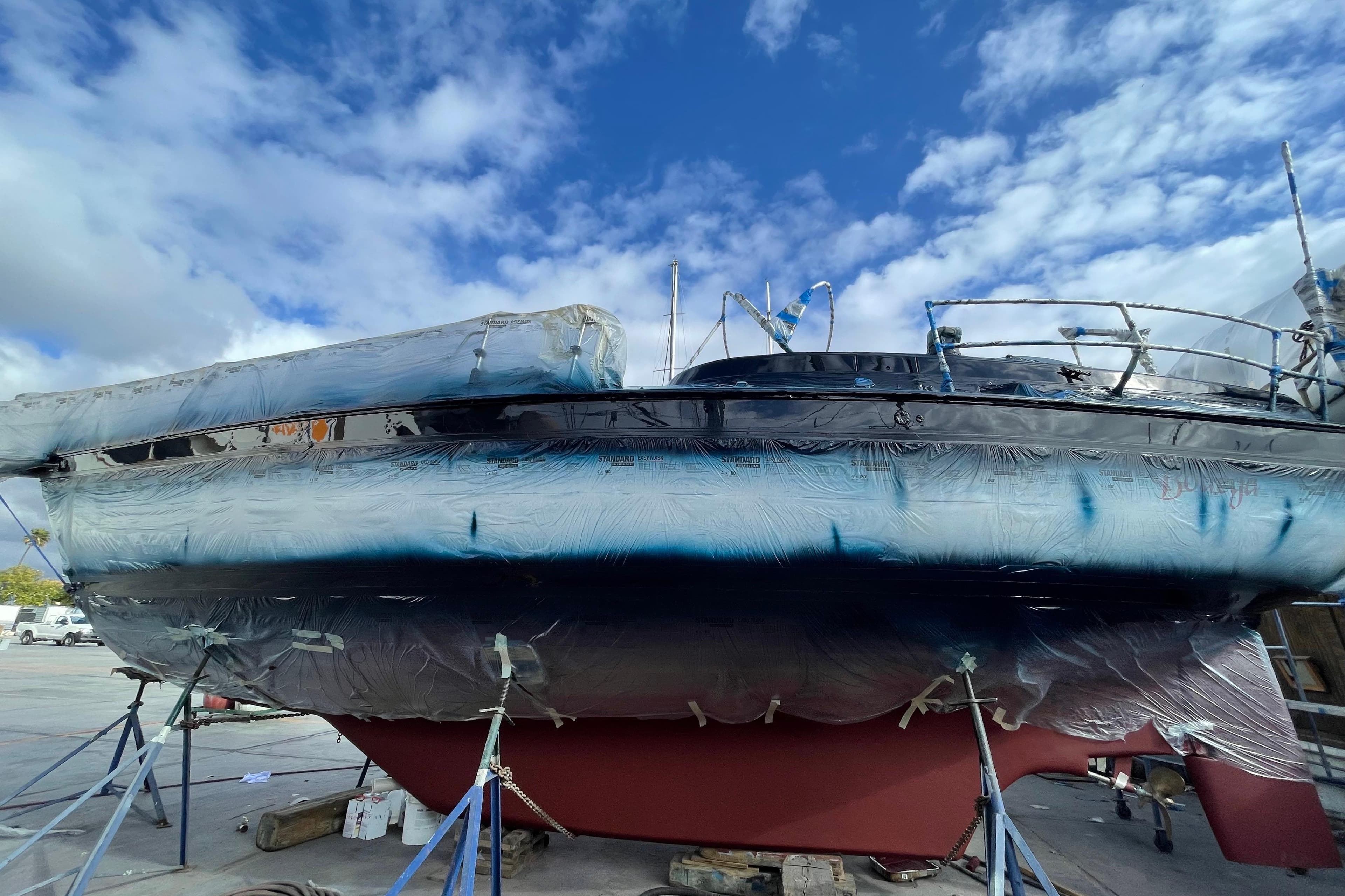 1982 Endeavour 37 sailboat undergoing maintenance, wrapped and elevated, under a partly cloudy sky.