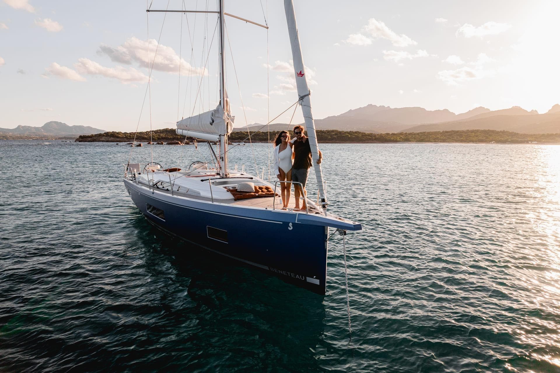 2025 Beneteau Oceanis 47 sailboat on serene water at sunset, with two people on deck.