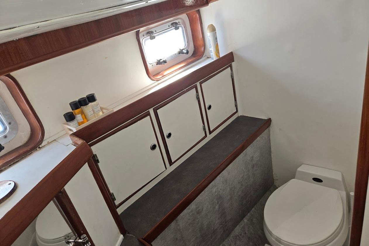 1982 Tayana Center Cockpit Cutter Ketch bathroom with wooden cabinets and porthole window.