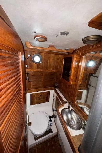 1986 Cabo Rico CB38 yacht bathroom with wooden interior, stainless steel sink, and porthole window.
