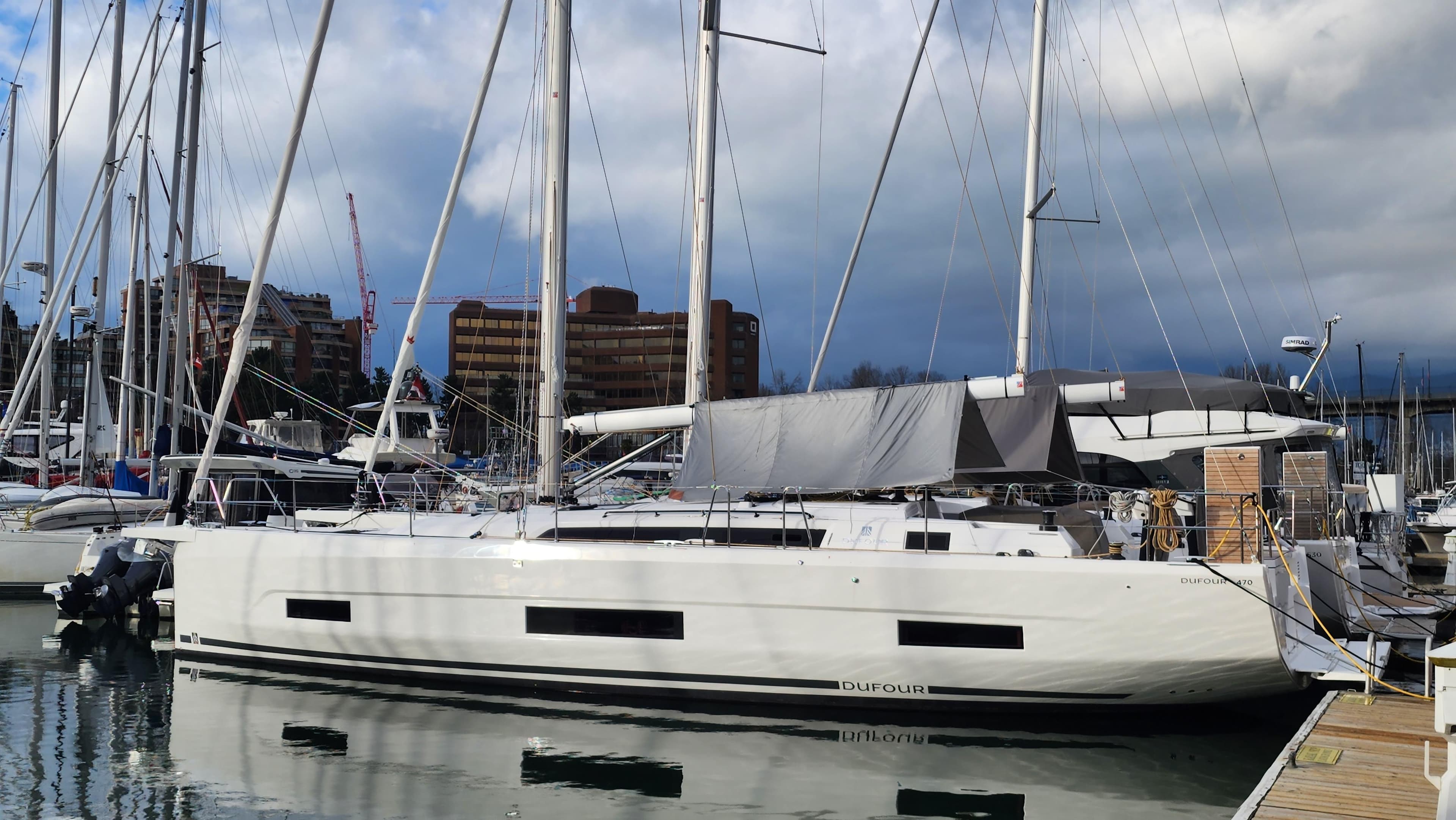 2023 Dufour 470 yacht docked in marina, surrounded by other sailboats.