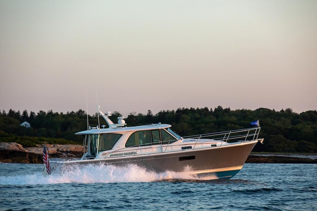 2026 Sabre 43 Salon Express cruising on water at sunset, with forested shoreline in background.