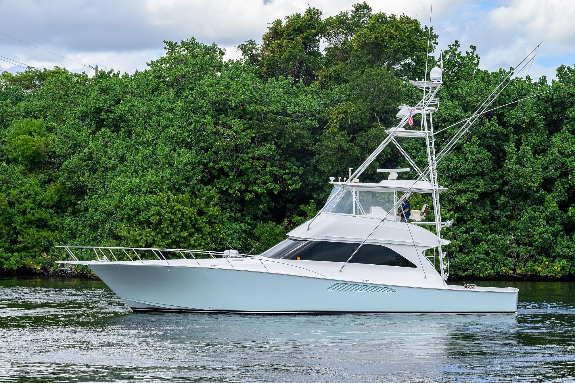 2004 Viking 56 Convertible yacht cruising near lush green shoreline.