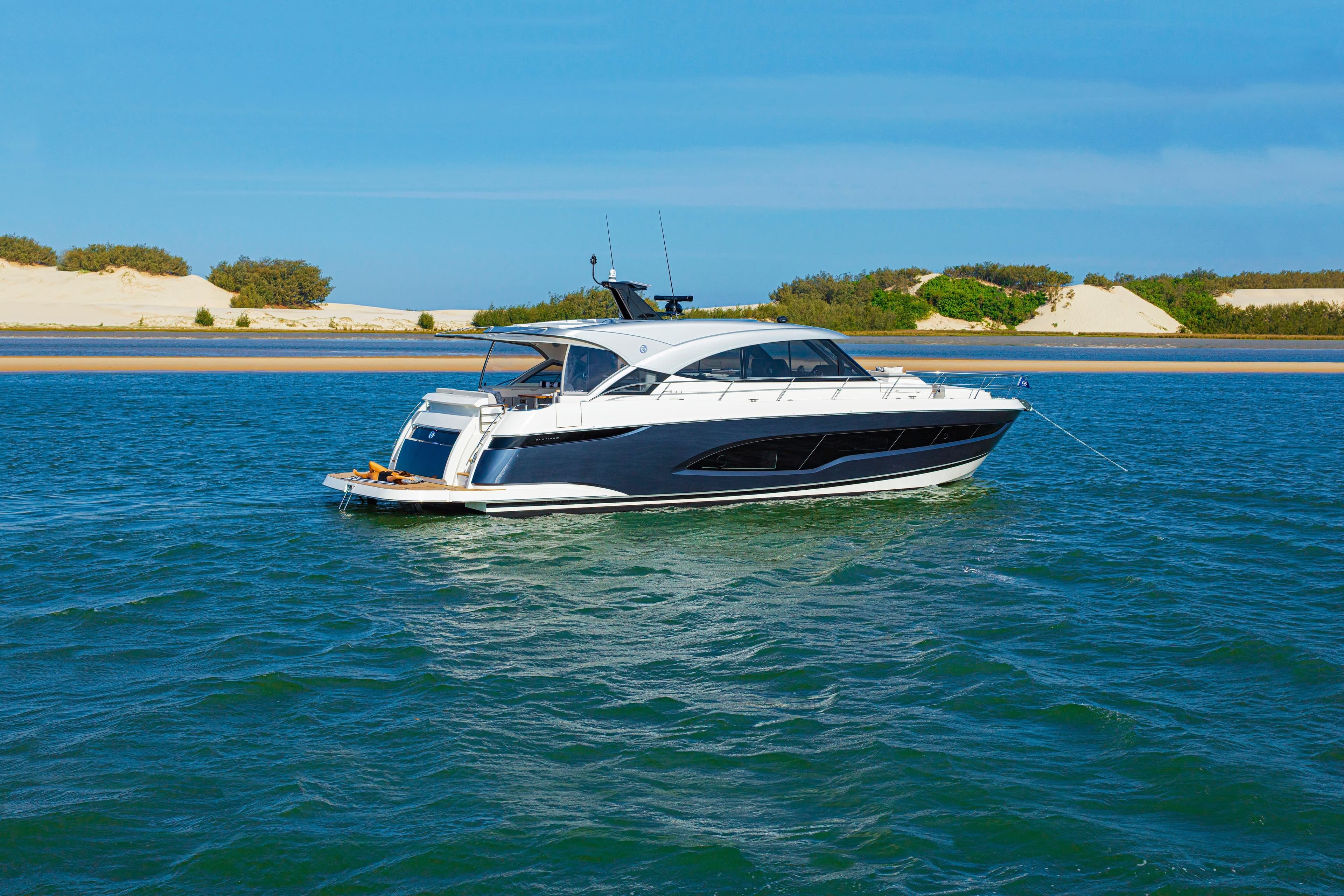 2026 Riviera 5600 Sport Yacht Platinum Edition cruising on blue waters near sandy shore.