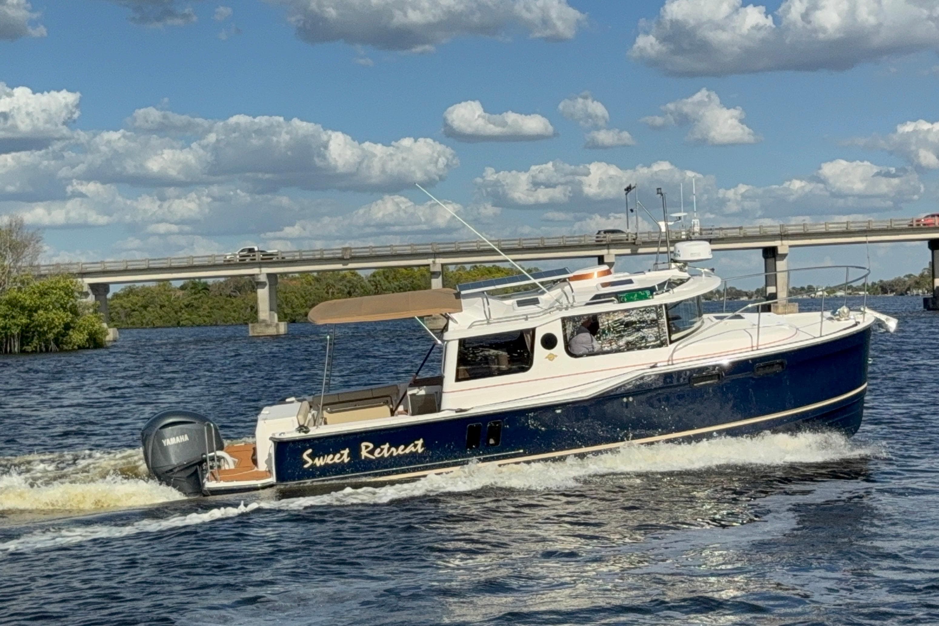 2022 Ranger Tugs R-27 boat cruising on a river under a cloudy sky.